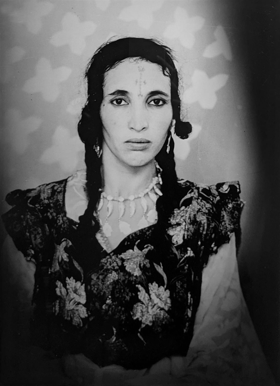 1960s black & white portrait of Amazigh woman with facial tattoos, wearing a black floral dress, in a photography studio