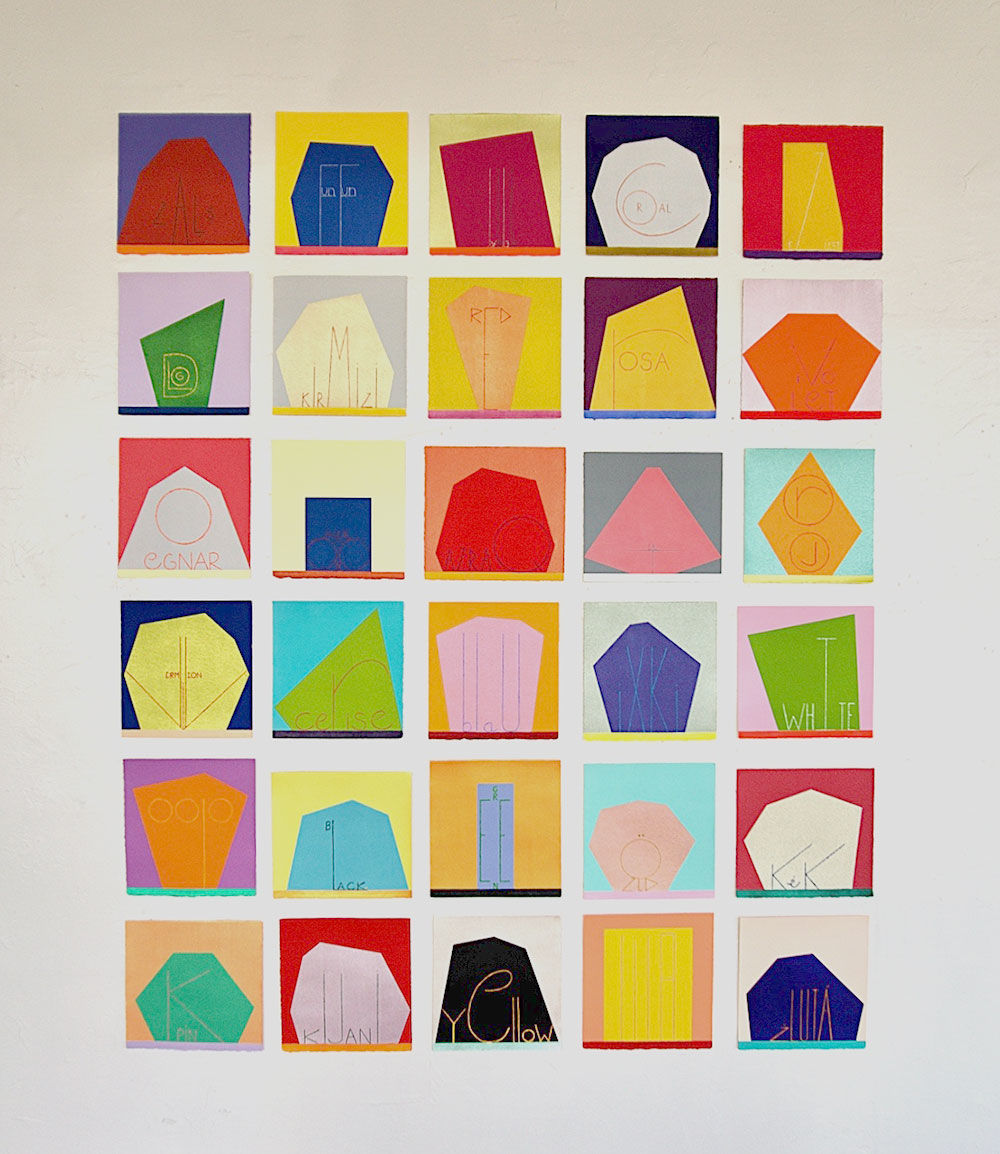 An array of colorful paintings comprised of geometric abstract forms displayed on a white wall
