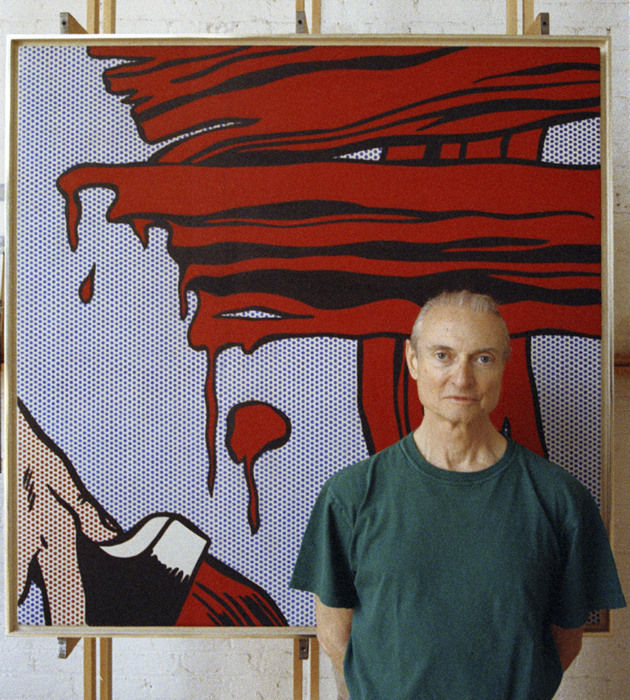 Photograph of a Roy Lichtenstein standing in front of a blue and red painting of a hand with a paintbrush