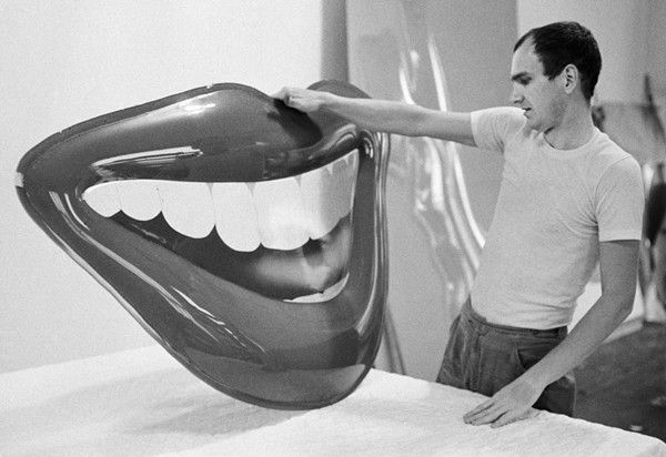 Black and white photograph of Tom Wesselmann in profile holding and looking at a sculpture of an open mouth
