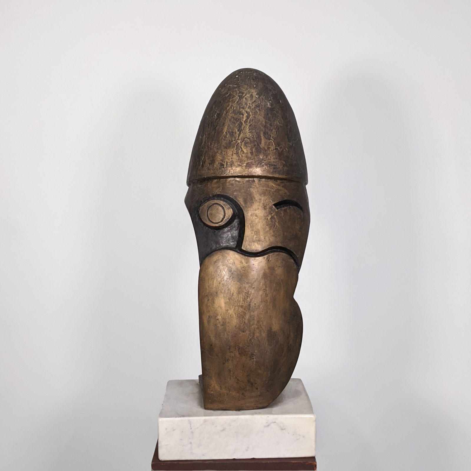 Brownish bronze sculpture of a stylized head with a hat, hollow, on marble pedestal
