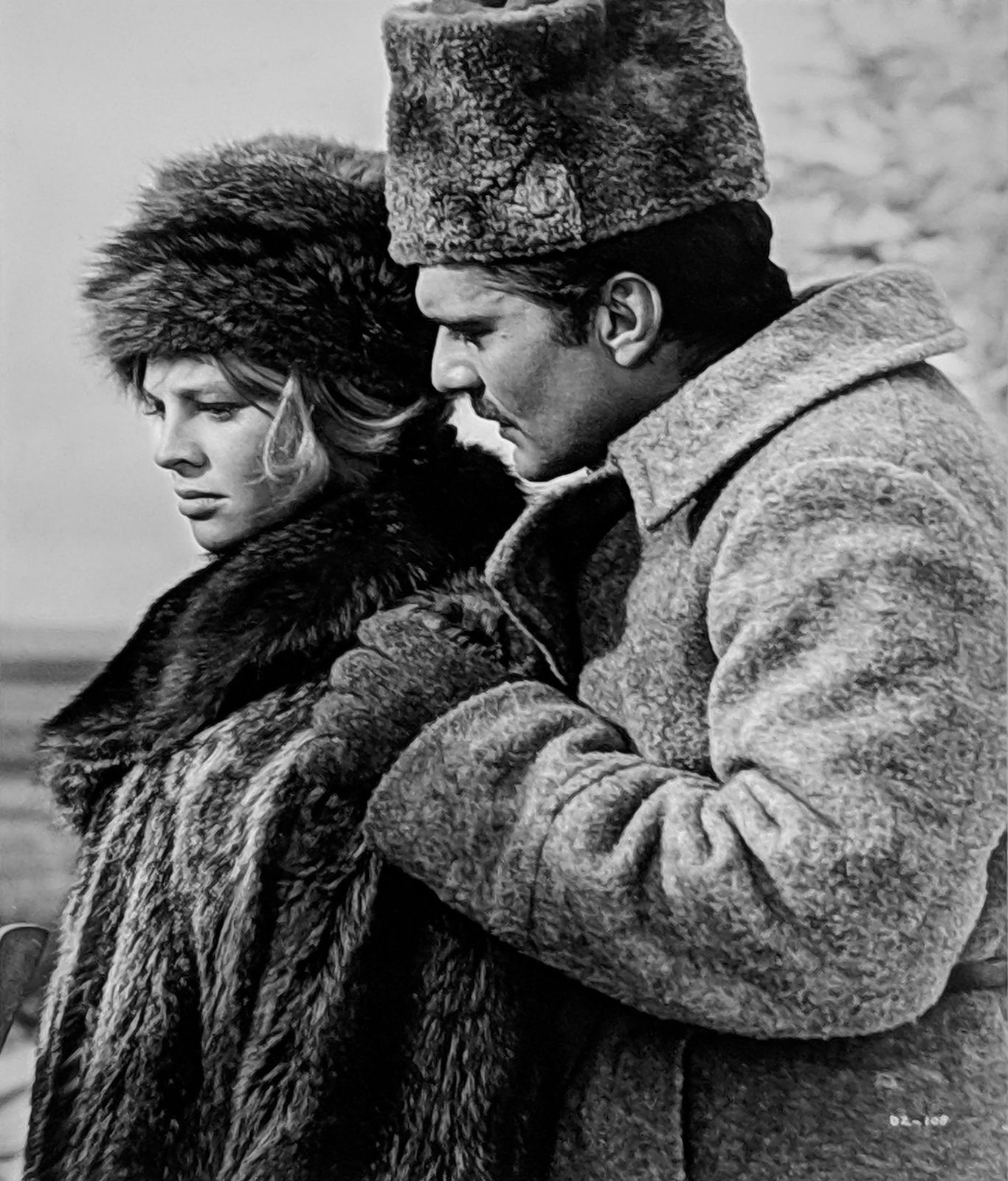 Black and white photograph of Julie Christie and Omar Sharif both in all fur winter outfits, Sharif holding Christie’s shoulders, outside on the set of “Doctor Zhivago”
