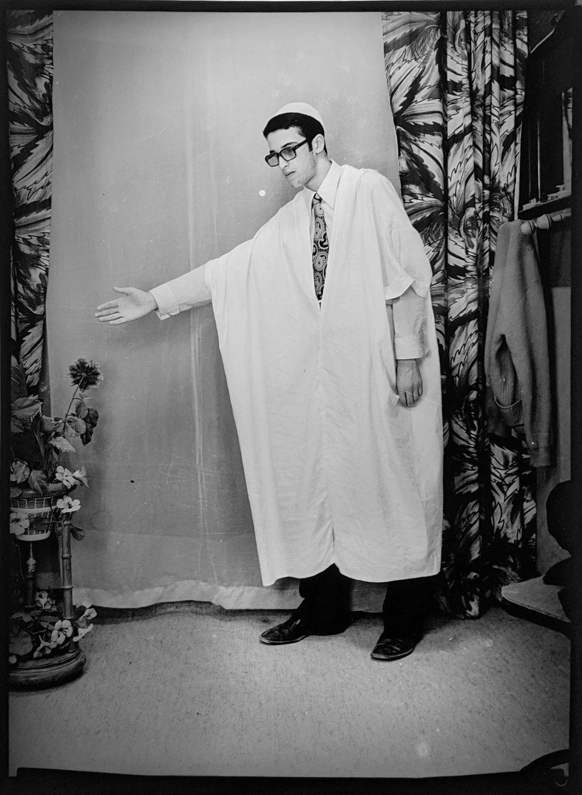 1960s black and white photograph of a man standing and gesturing to the left in traditional Algerian attire