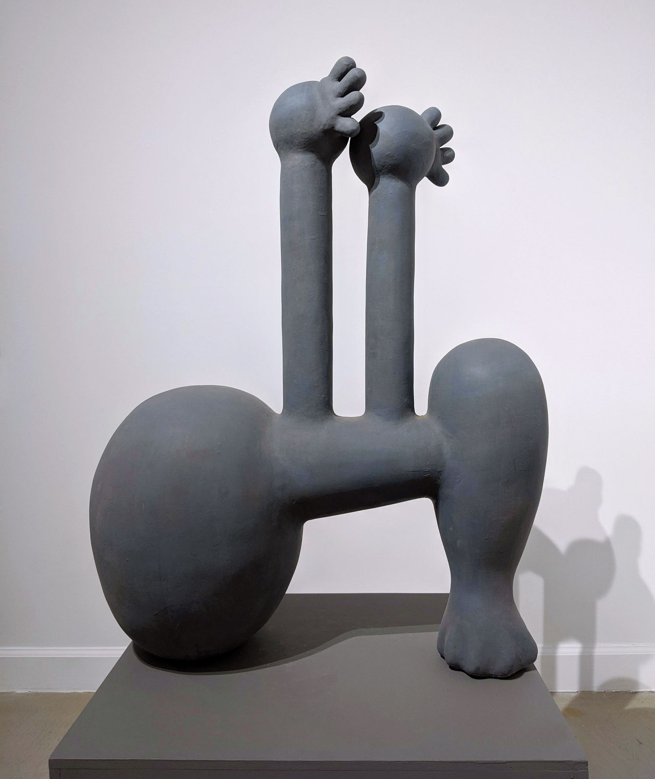 Dark gray abstract terra cotta sculpture with cylindrical and bulbous elements suggesting hands and feet