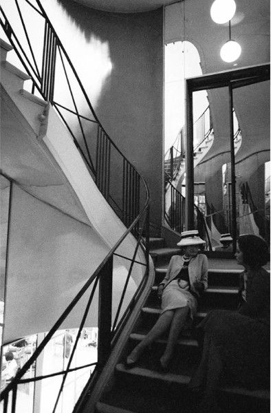Black and white photograph of Designer Coco Chanel sitting on a winding staircase surrounded by mirrors