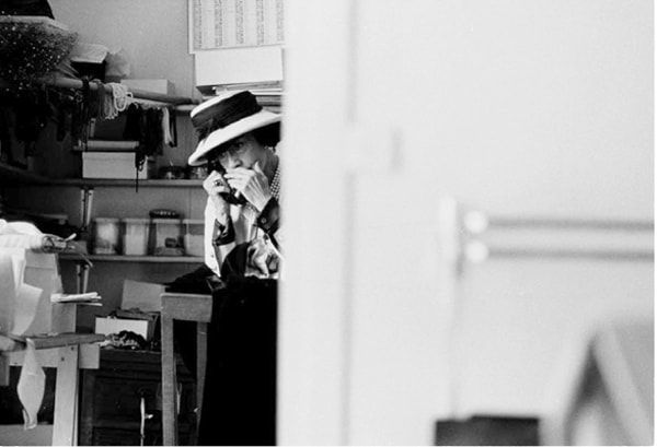 Black and white photograph of Designer Coco Chanel on the phone in her atelier, mostly obscured by a door