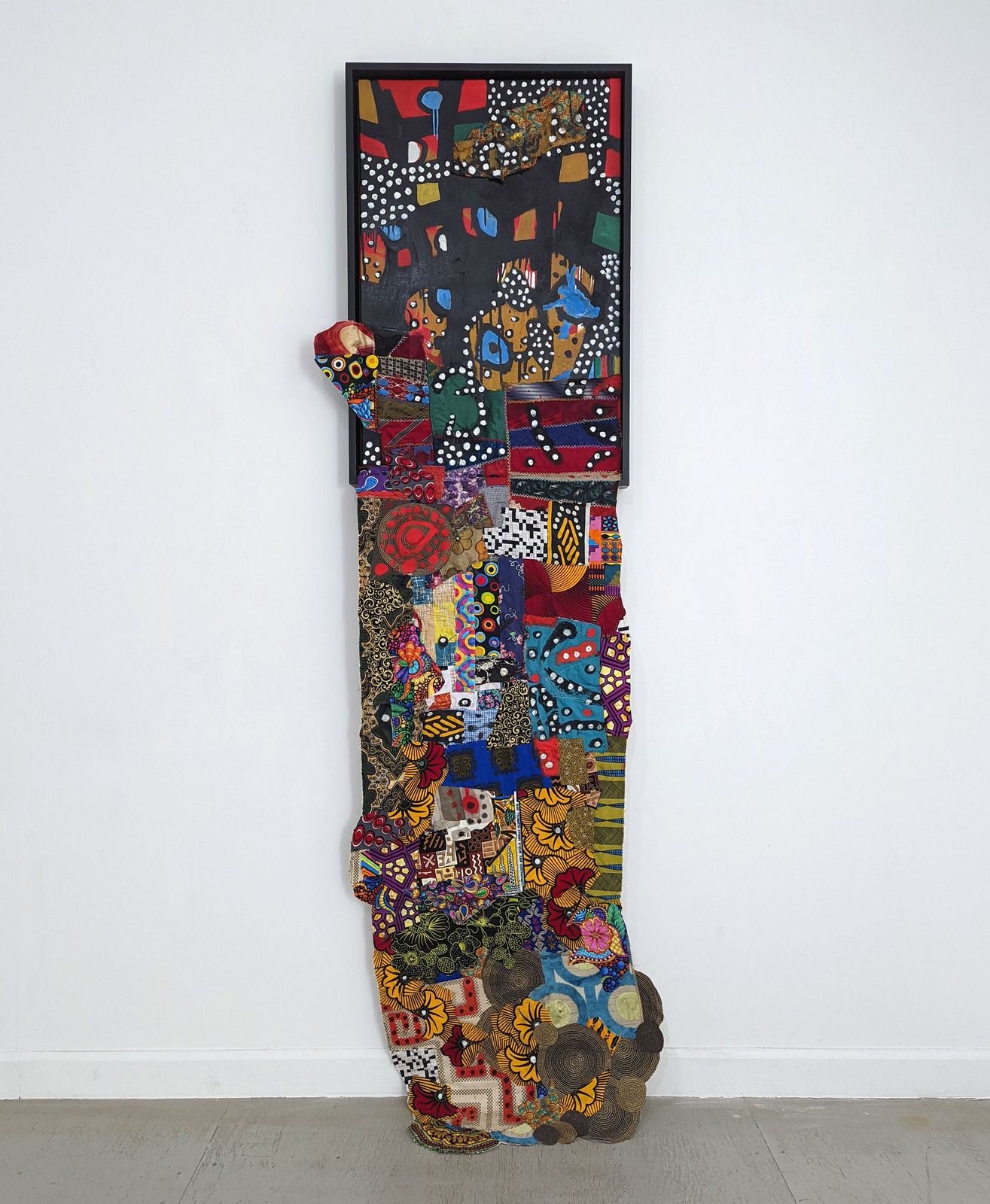 Colorful artwork comprised of oil paint and patterned fabric extending past the bottom of the canvas in a 