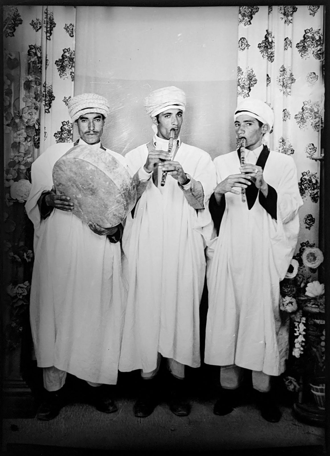 1960s black and white photograph of three boys in traditional algerian attire with white head scarves in a photography studio