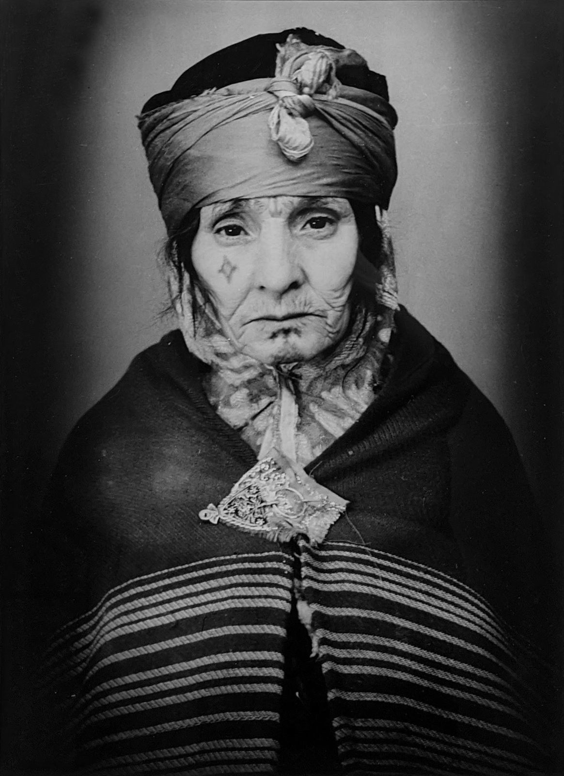 1960s black & white portrait of Amazigh woman with facial tattoos, wearing striped outfit, in a photography studio