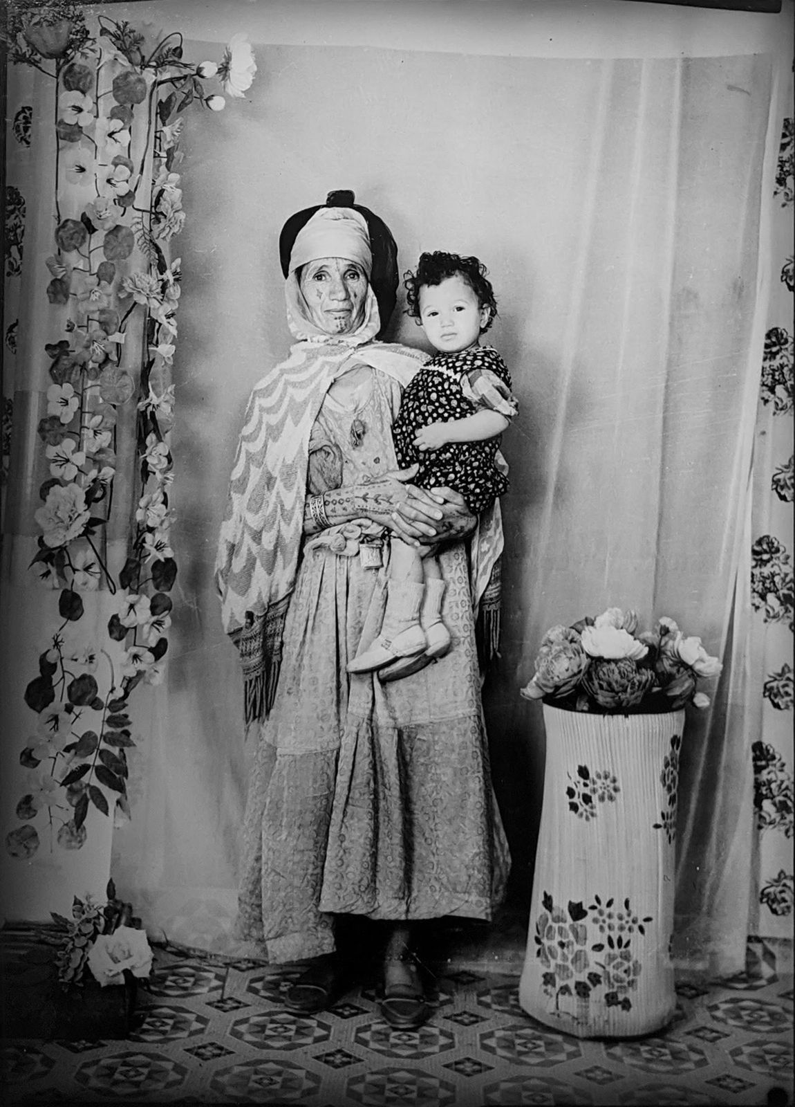 1960s black and white photograph a woman holding a child in her arms in traditional algerian attire