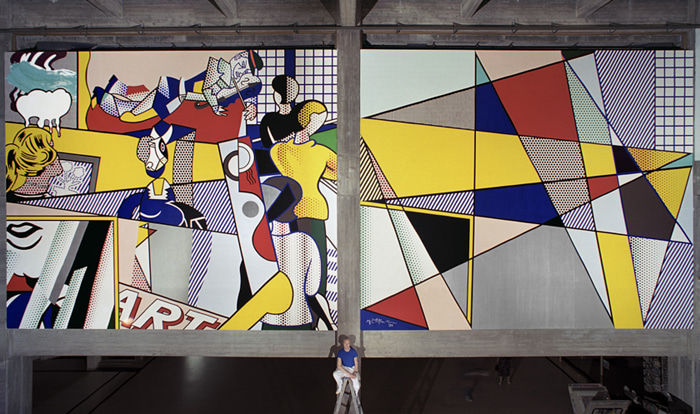 Photograph of Roy Lichtenstein sitting on a ladder in front of a multicolored mural of figures and geometric designs