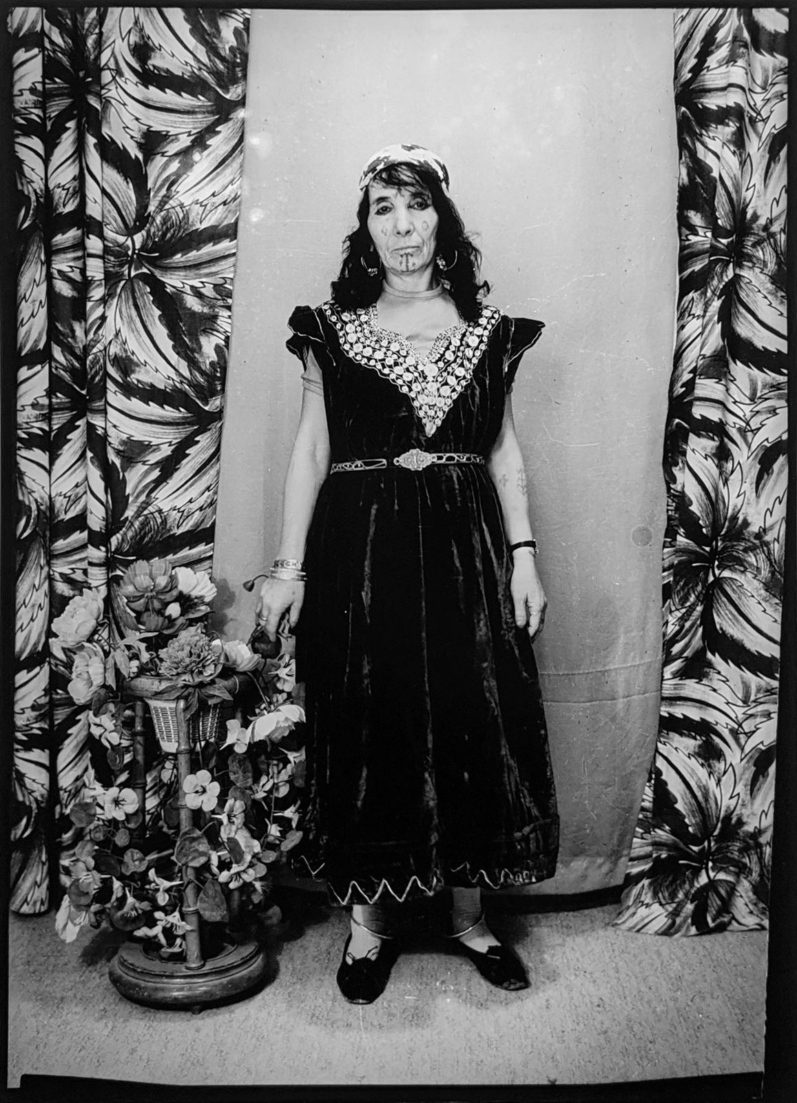 1960s black and white photograph of a woman standing in a black embroidered dress with her hair loose
