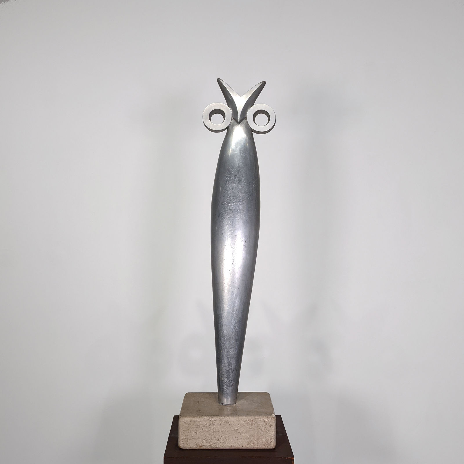 Modernist polished aluminum sculpture of vertical owl with stylized eyes and head, on brown marble base
