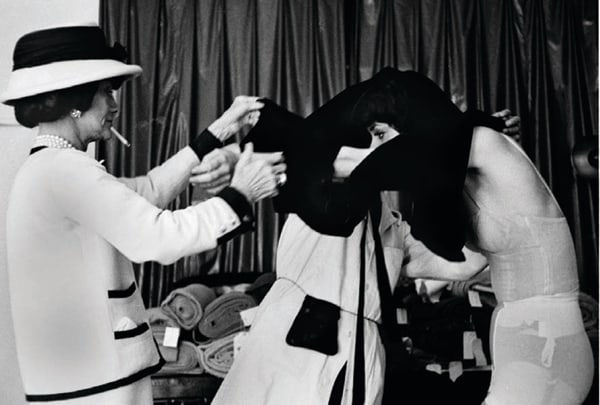 Black and white photograph of Designer Coco Chanel helping a model undress