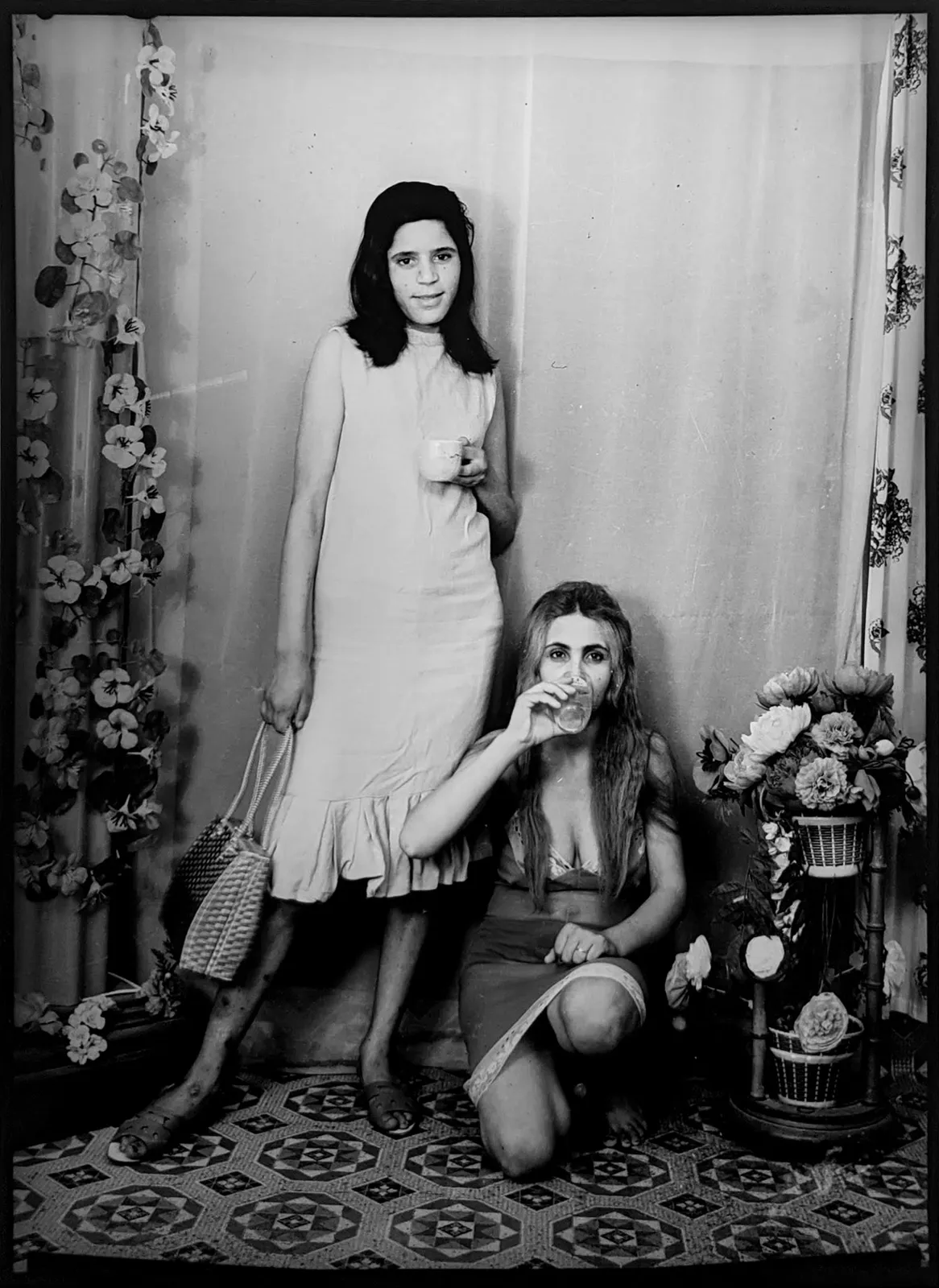 1960s black & white photograph of two women, one crouching, one standing, in a photography studio