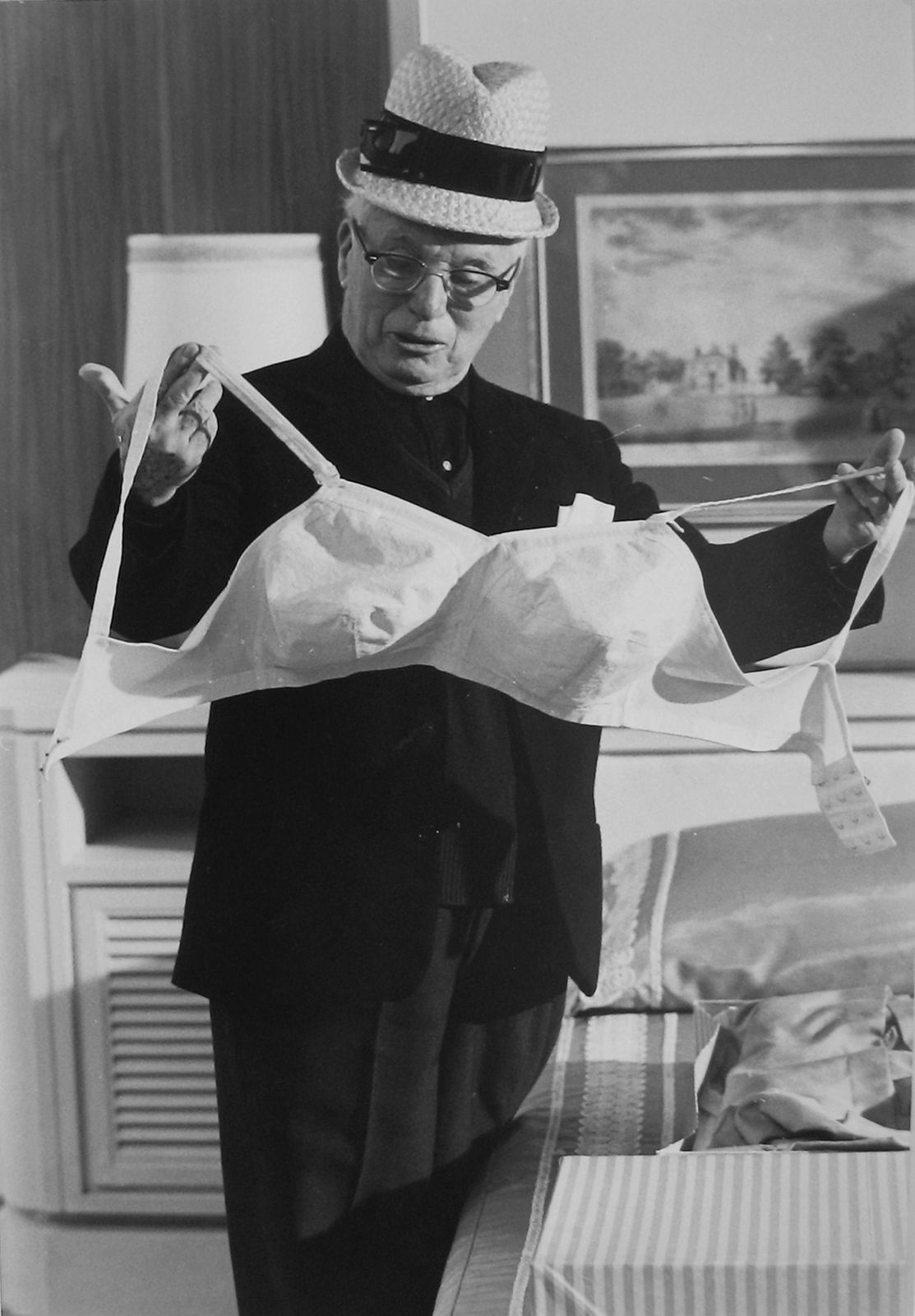 Black and white photograph of Charlie Chaplin holding a large white bullet bra on the set of “A Countess from Hong Kong”