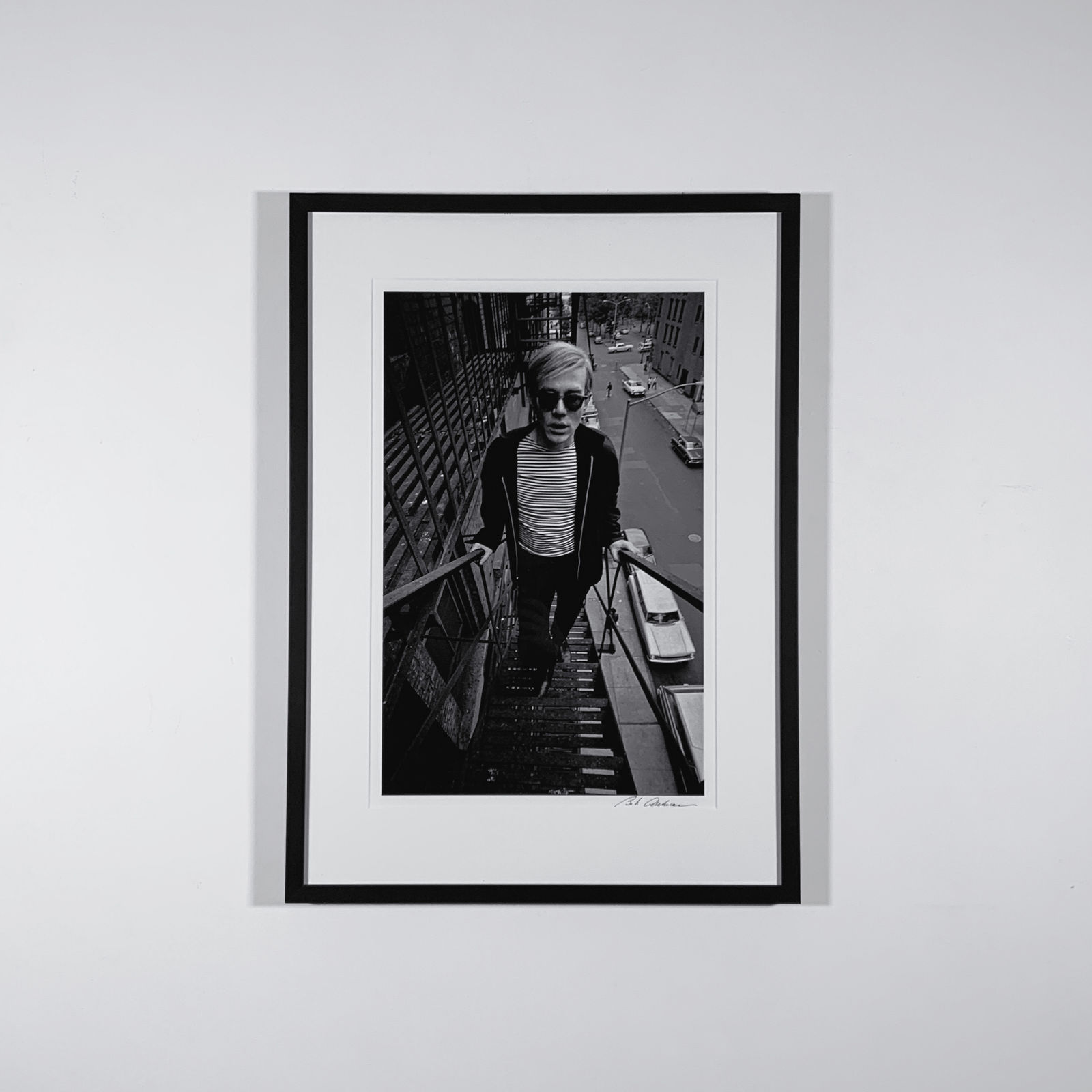 Framed Black and white photograph of Andy Warhol in a Breton striped shirt and sunglasses ascending a fire escape above a city street