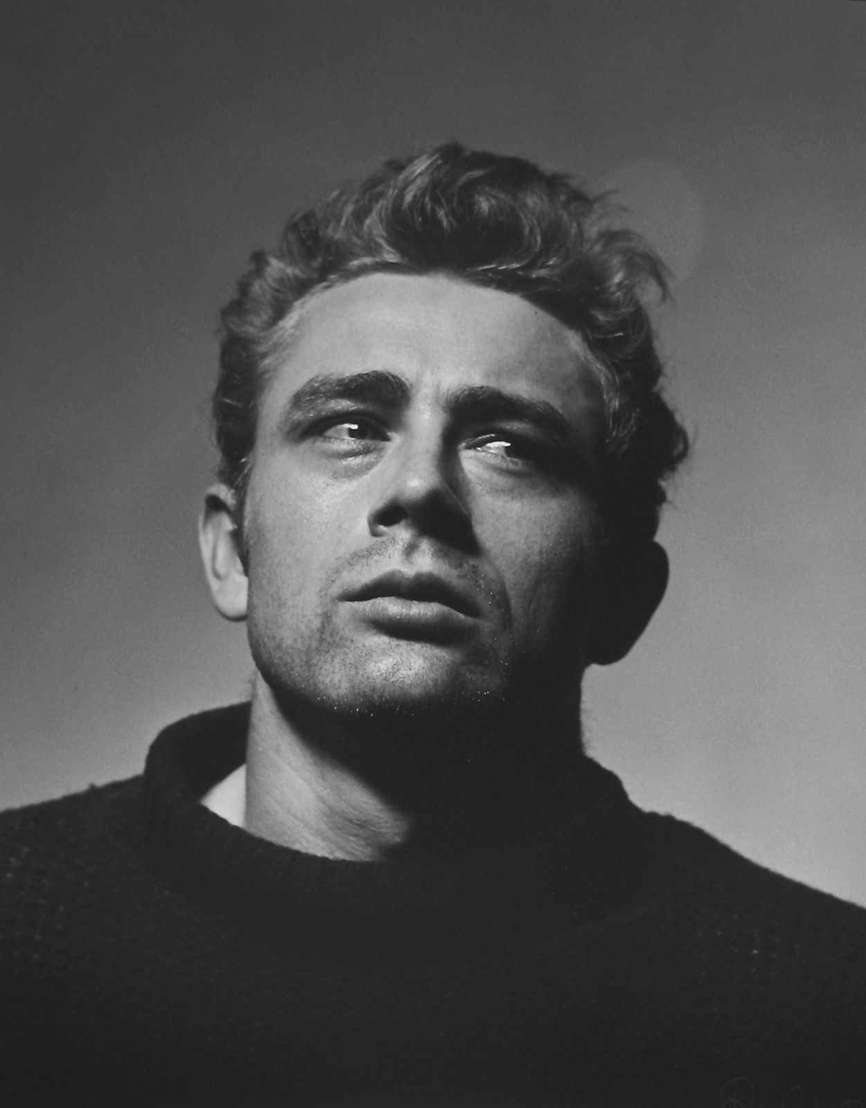 Black and white portrait photograph of James Dean with a sideways glance from a slightly lower vantage point