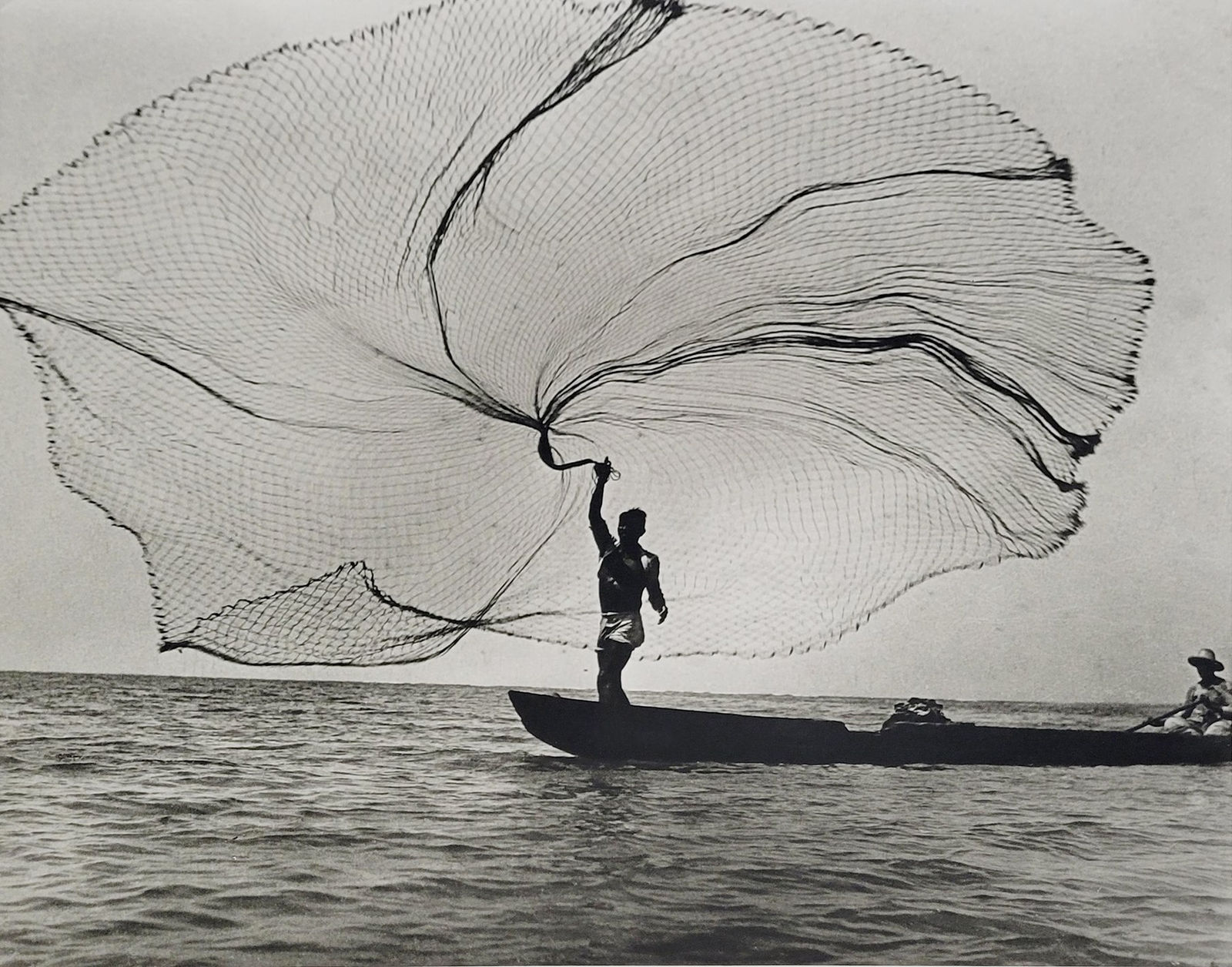Black and white photograph of the silhouette of a fisherman casting a net off of a boat in Magdalena, Colombia