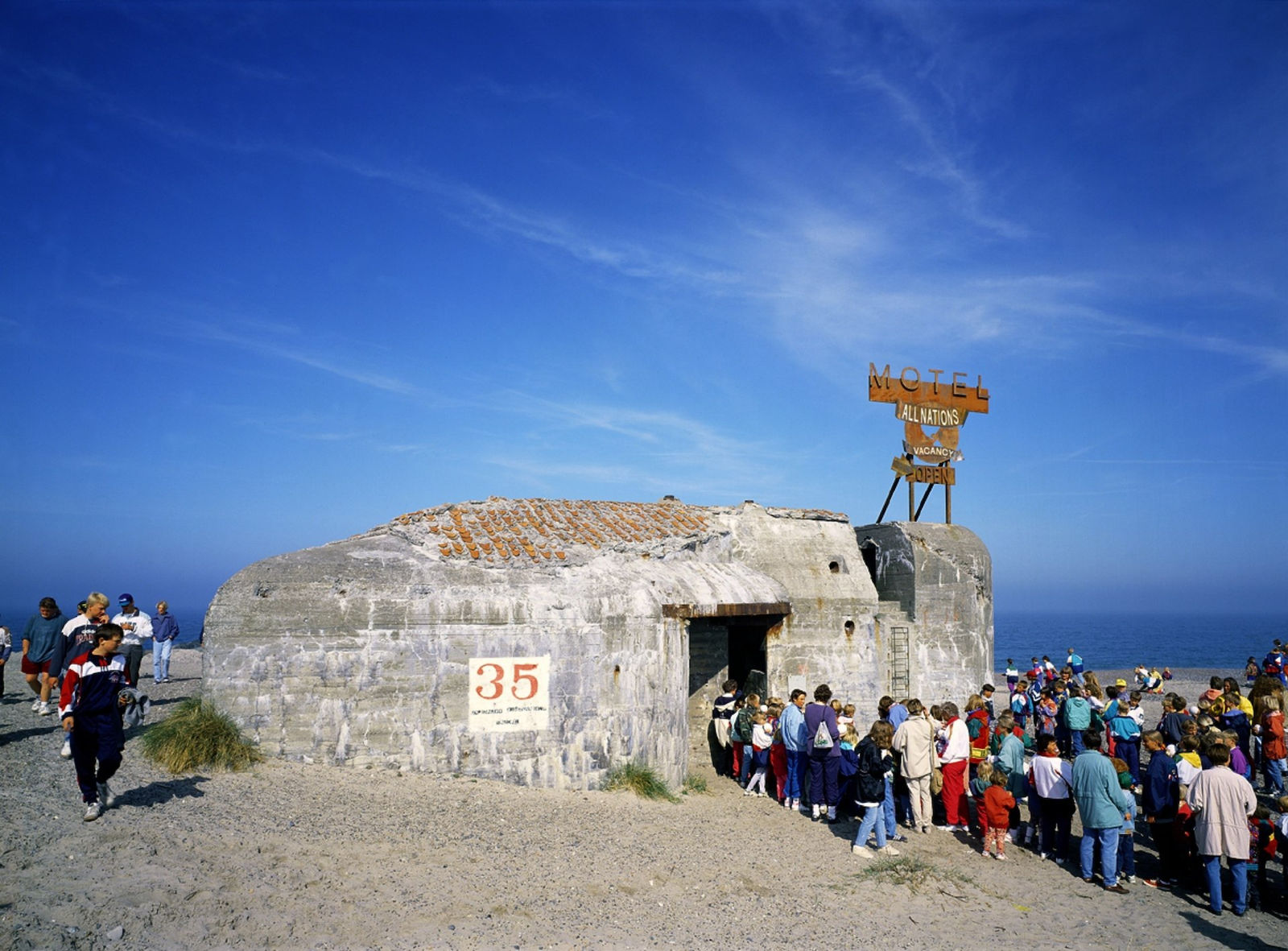 Art installation, crowd of people entering a World War 2 bunker with sign that reads “Bunker Motel”