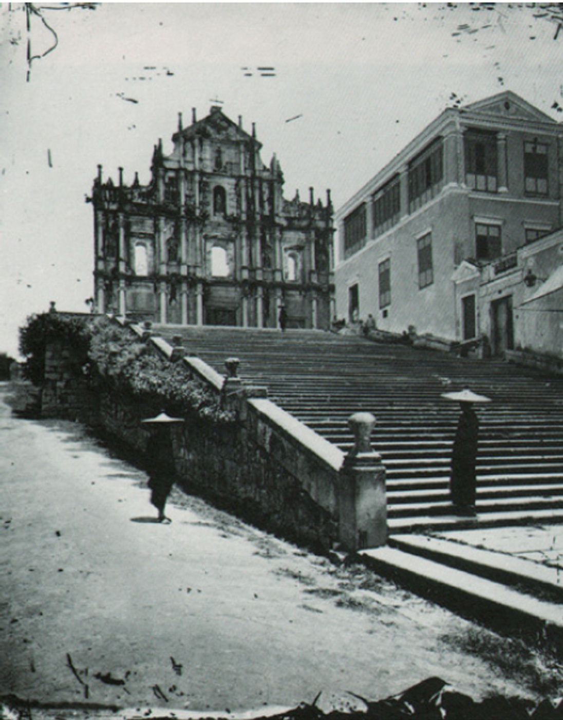 View of the frontage of a destroyed church, with steps and two Asian men with hats