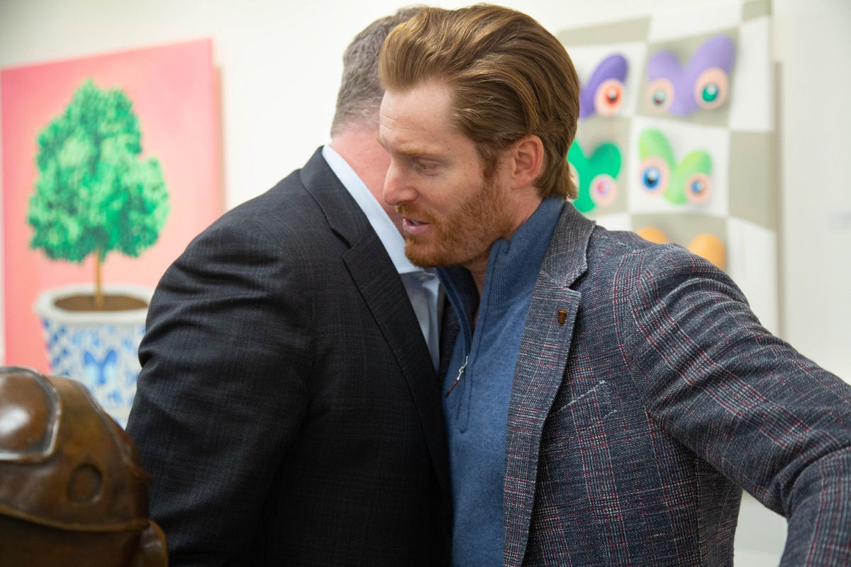 Men hugging in front of paintings created by John Westbay displayed in Carousel Fine Art's Atlanta gallery space during the spotlight exhibition for John Westbay titled "Love, Outside the Lines."