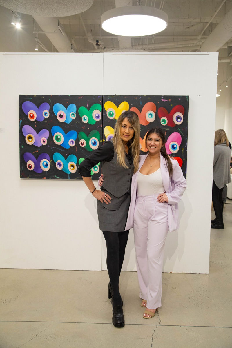 Women posing in front of painting by John Westbay in Carousel Fine Art's Atlanta gallery space during the spotlight exhibition for John Westbay titled "Love, Outside the Lines."