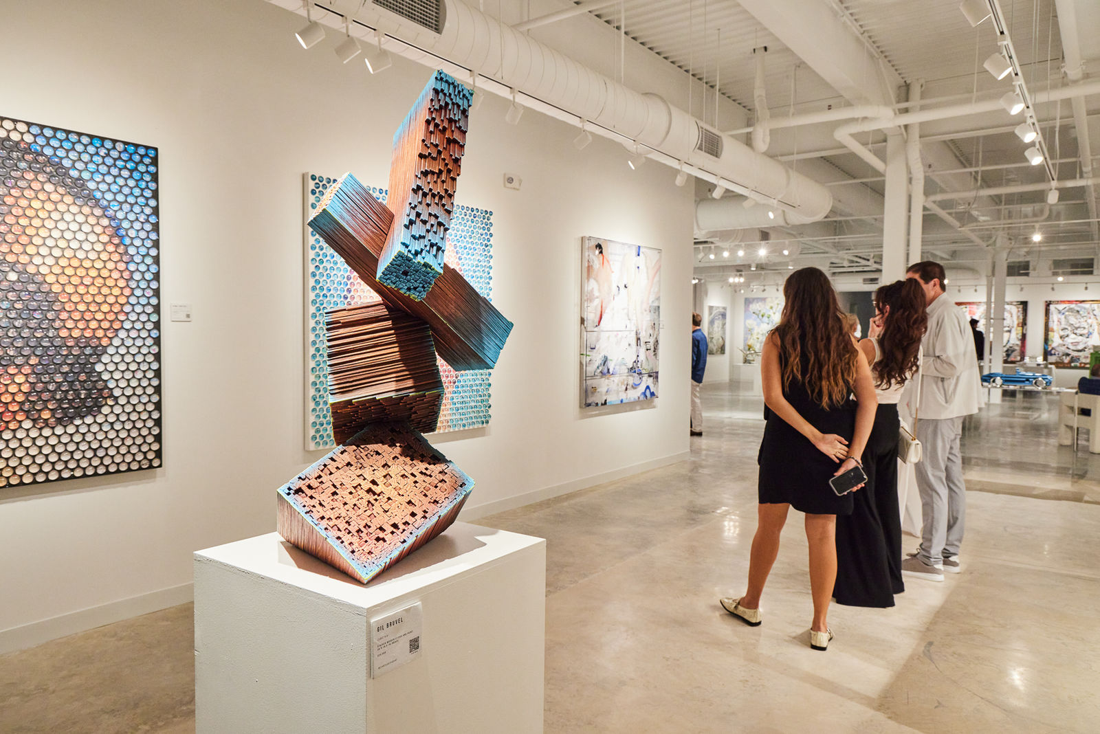 Wooden sculpture by Gil Bruvel in front of gorgeous floral works by Eric Alfaro.