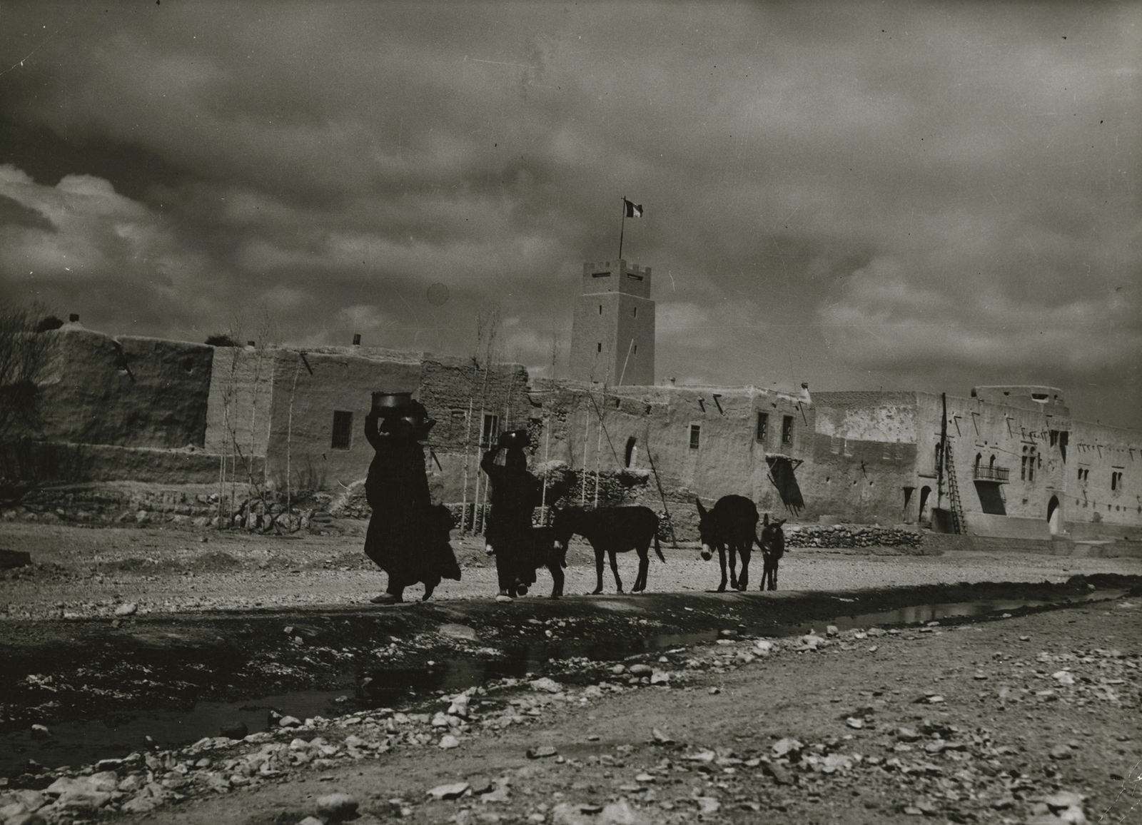Margaret Bourke-White, Women carrying water containers on their heads as they lead mules along the road outside native Bedouin camel cavalrymen´s garrison, Poste Veillotte, in desert village near Damascus, Syria, 1940