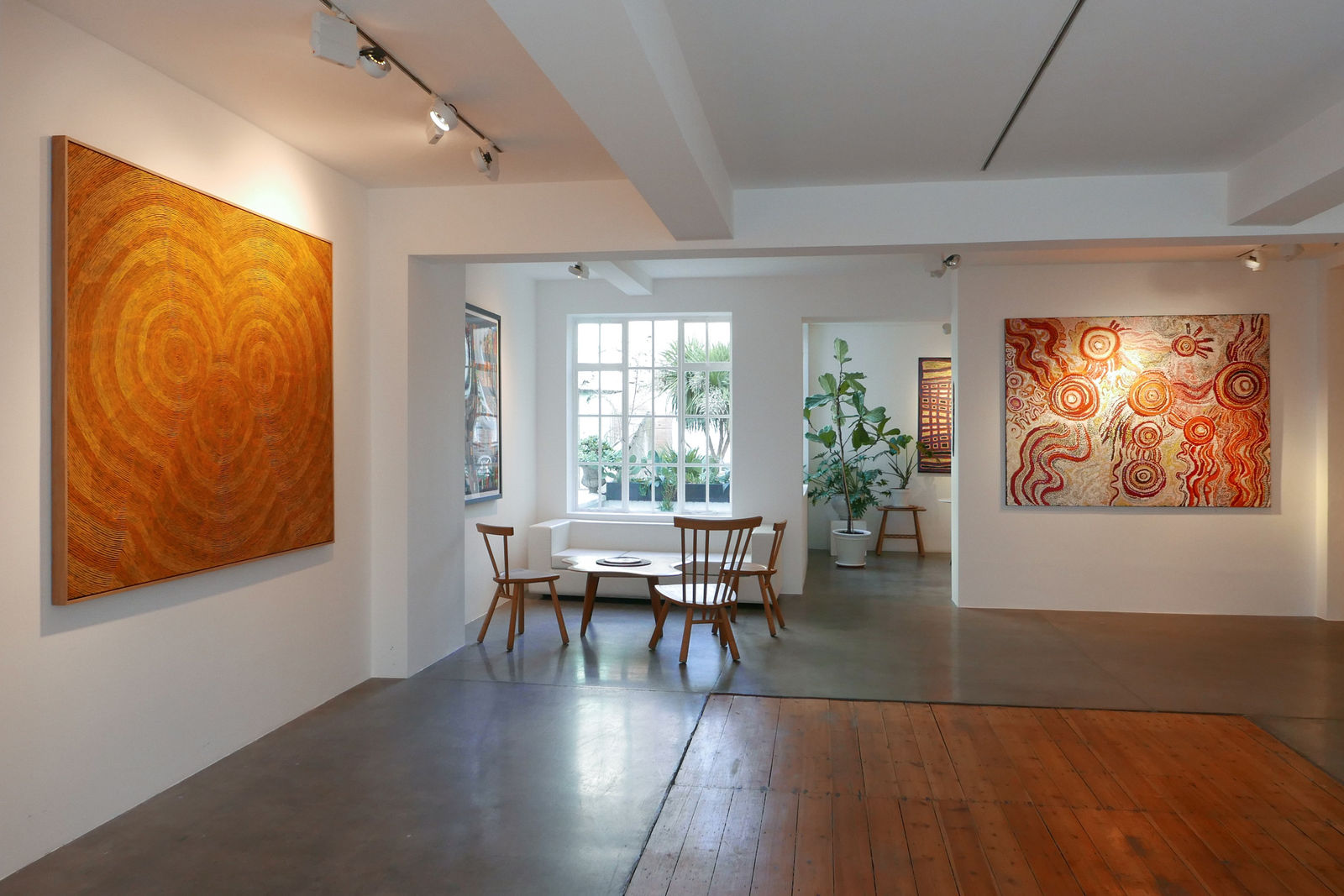 A wide-angle view of the second-floor of the Rebecca Hossack Art Gallery. Large Aboriginal artwork adorns the walls whilst a large window lights a coffee table in a corner of the room.