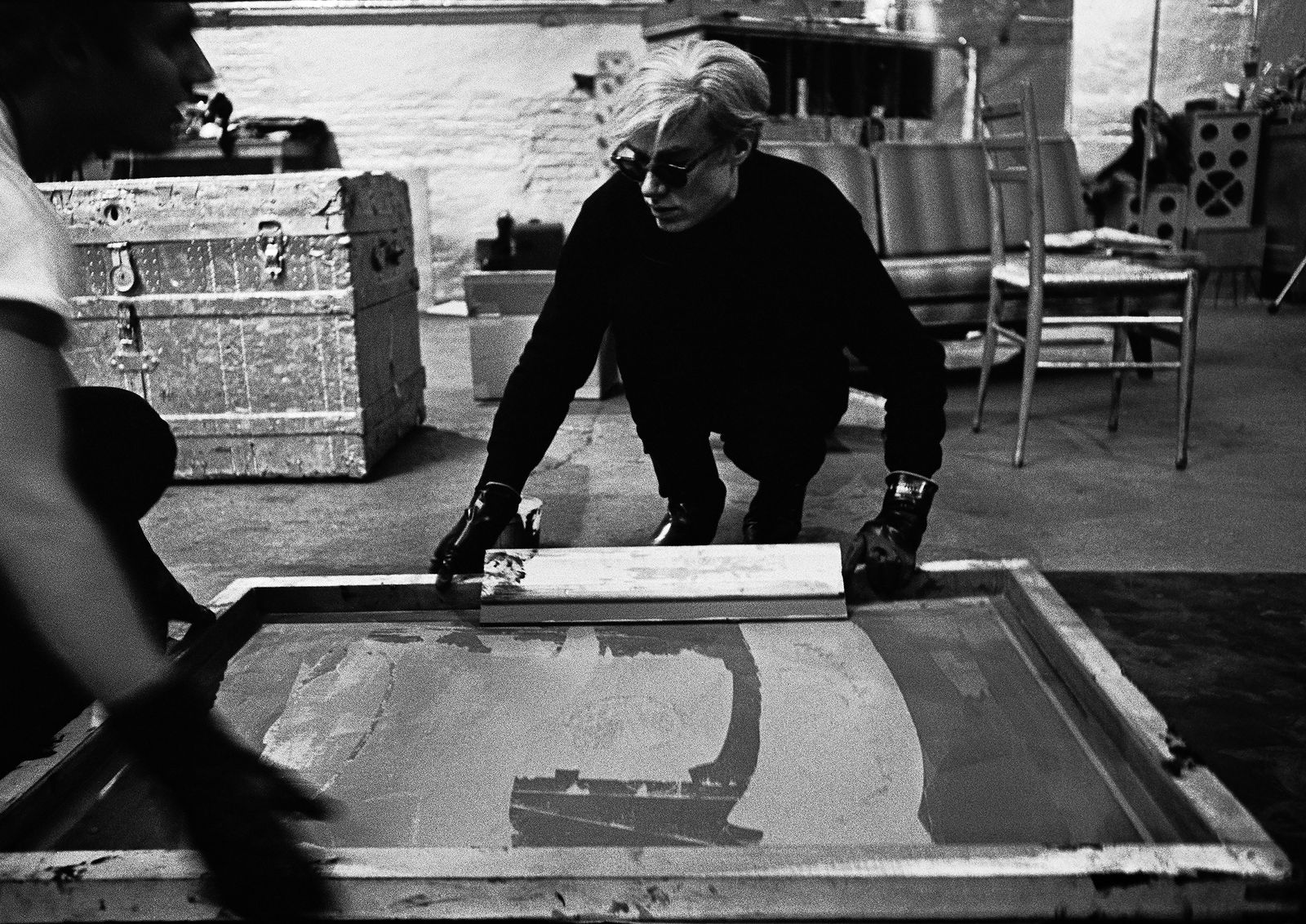 Andy Warhol working with Gerard Malanga on the Campbell’s Soup paintings at the Factory, New York, 1964. Photo Ugo Mulas © Ugo Mulas Heirs. All rights reserved. Andy Warhol Artwork © 2023 The Andy Warhol Foundation for the Visual Arts, Inc.