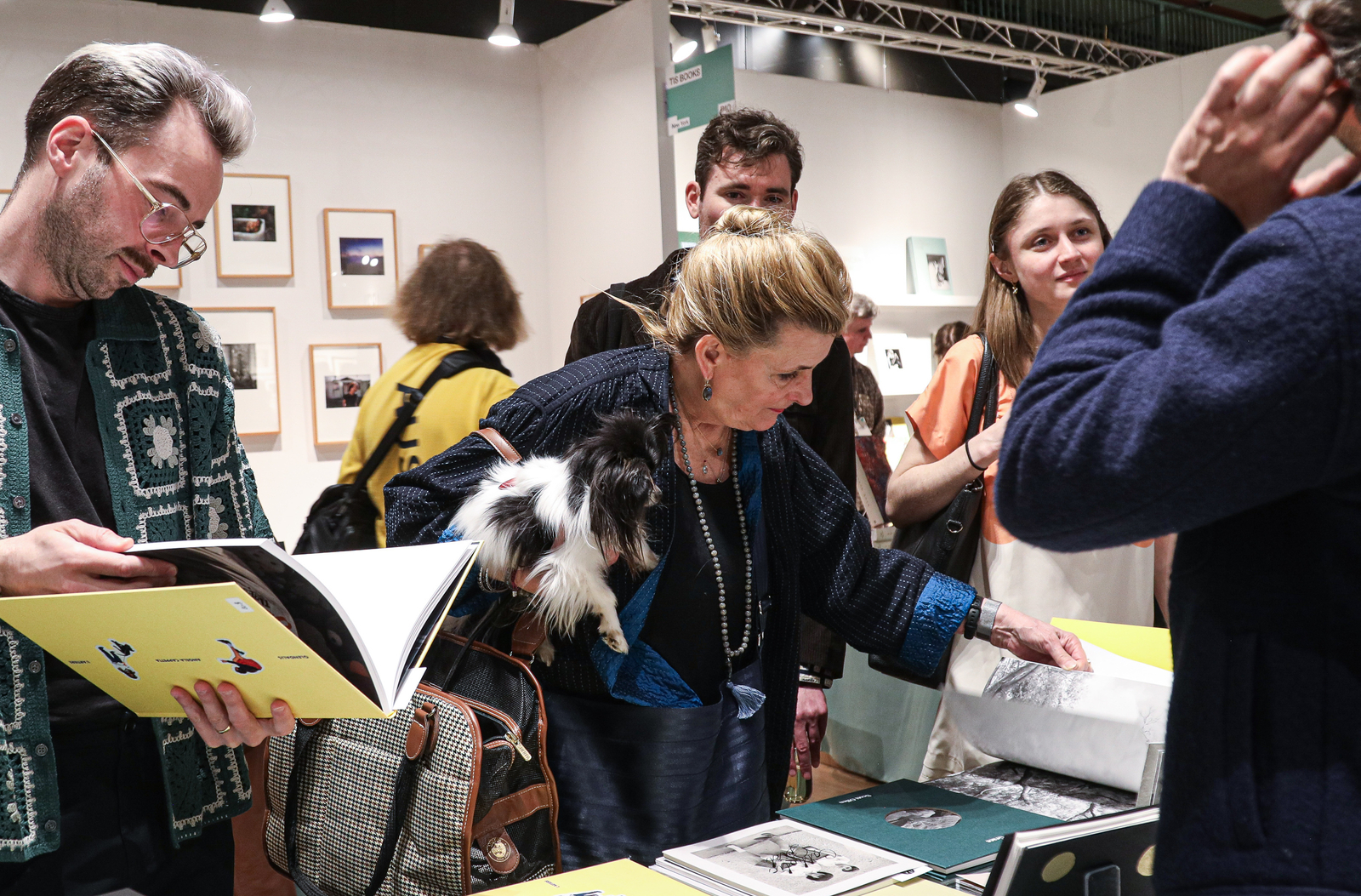 People look at photo books at the fair; one person holds a dog.