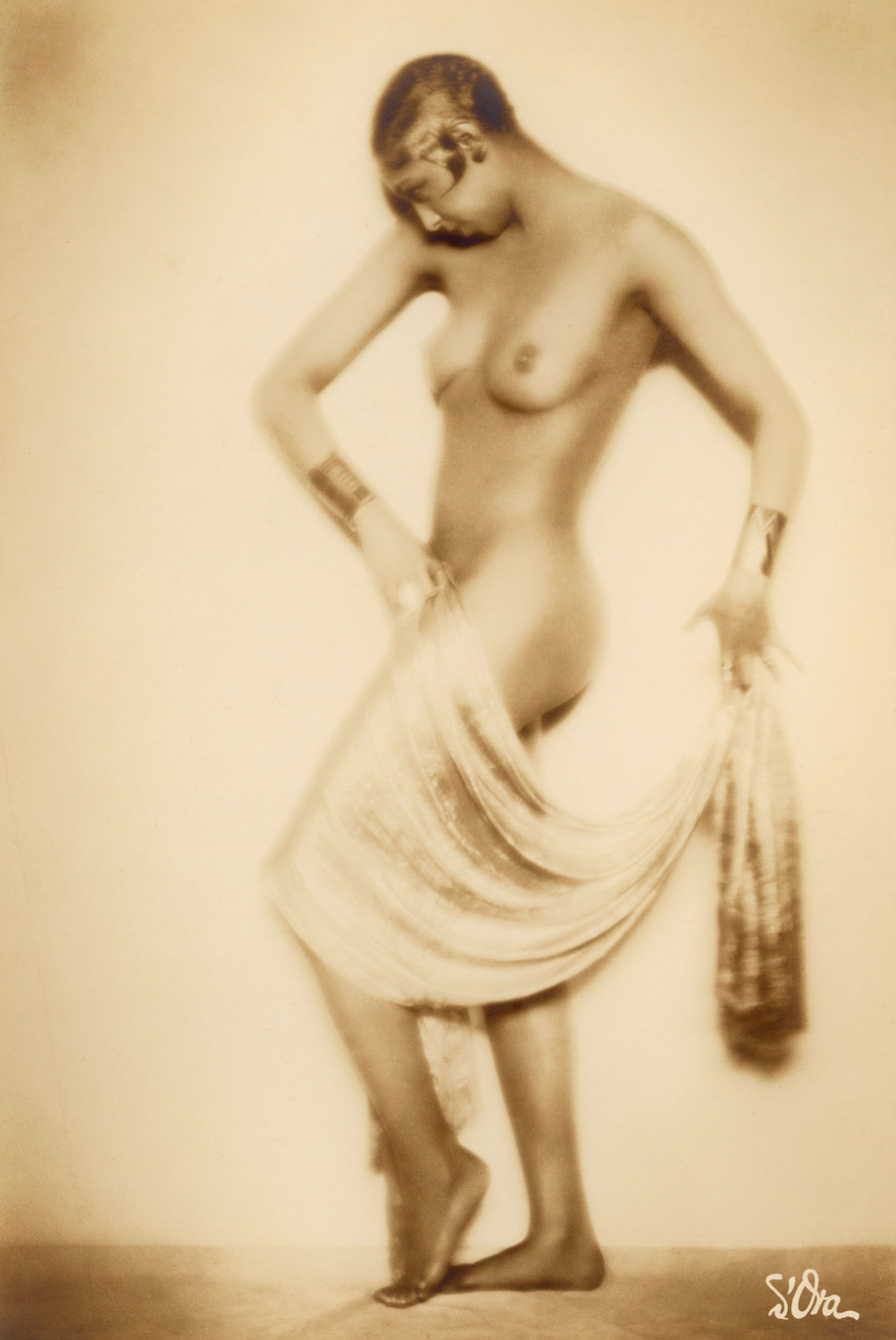 A nude Josephine Baker strikes an artful geometric pose while holding a swath of fabric draped over her leg.