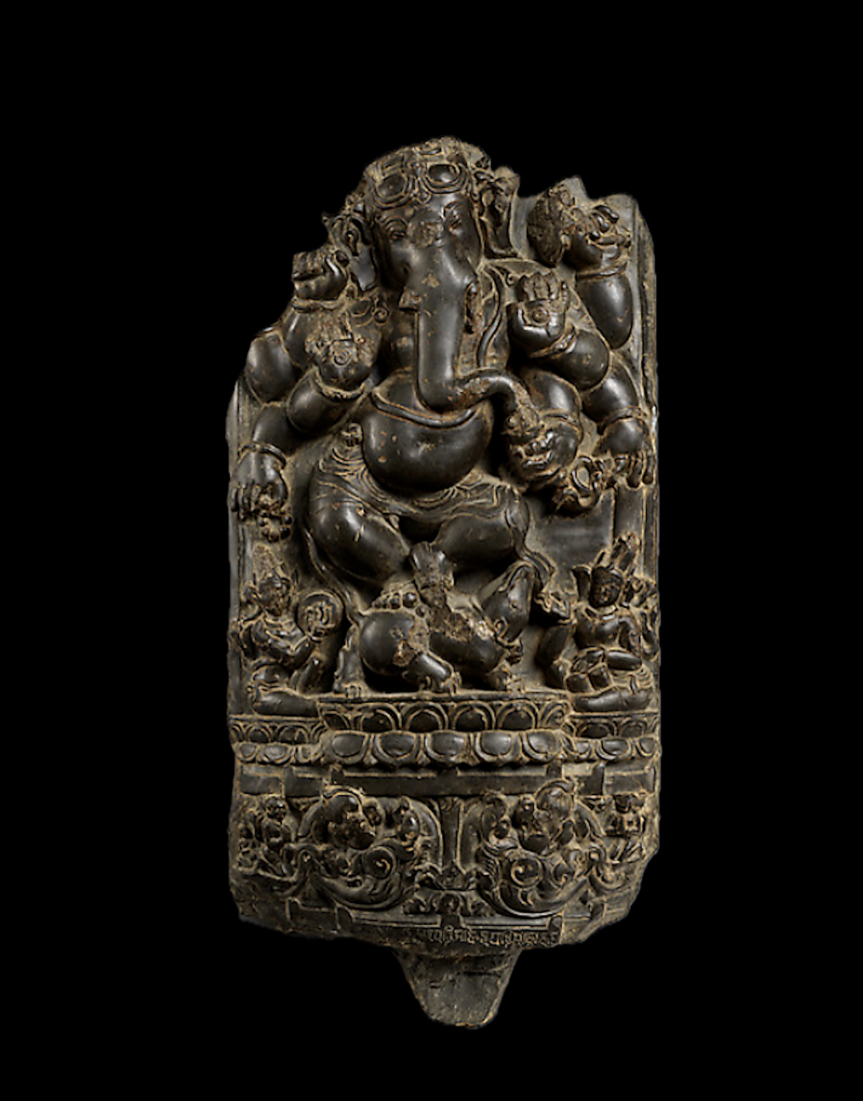 This finely-carved stone relief depicts Ganesha, the elephant-headed son of Shiva, dancing in a compact yet animated posture within a vertically-framed niche.