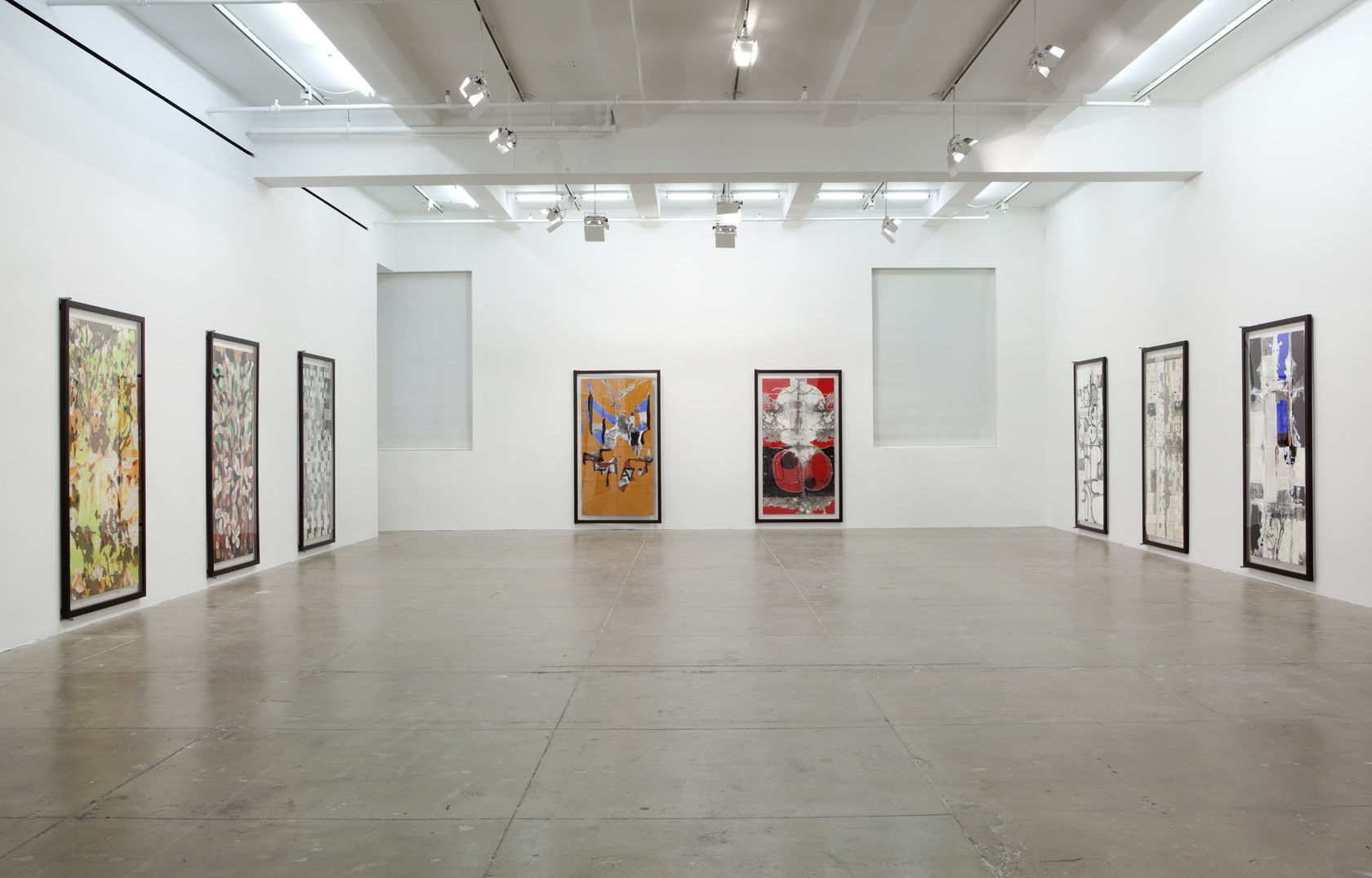 Eight large vertical abstract paintings fill the walls of a large white room. 