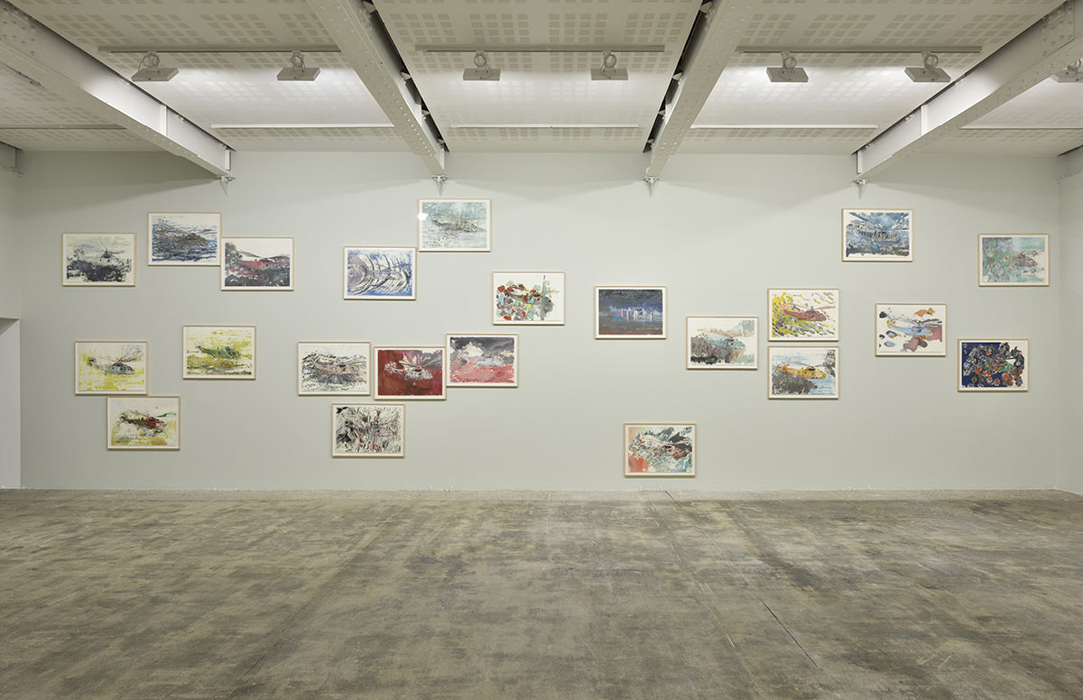 Framed paintings of helicopters on paper hang at various heights on a beige wall. 
