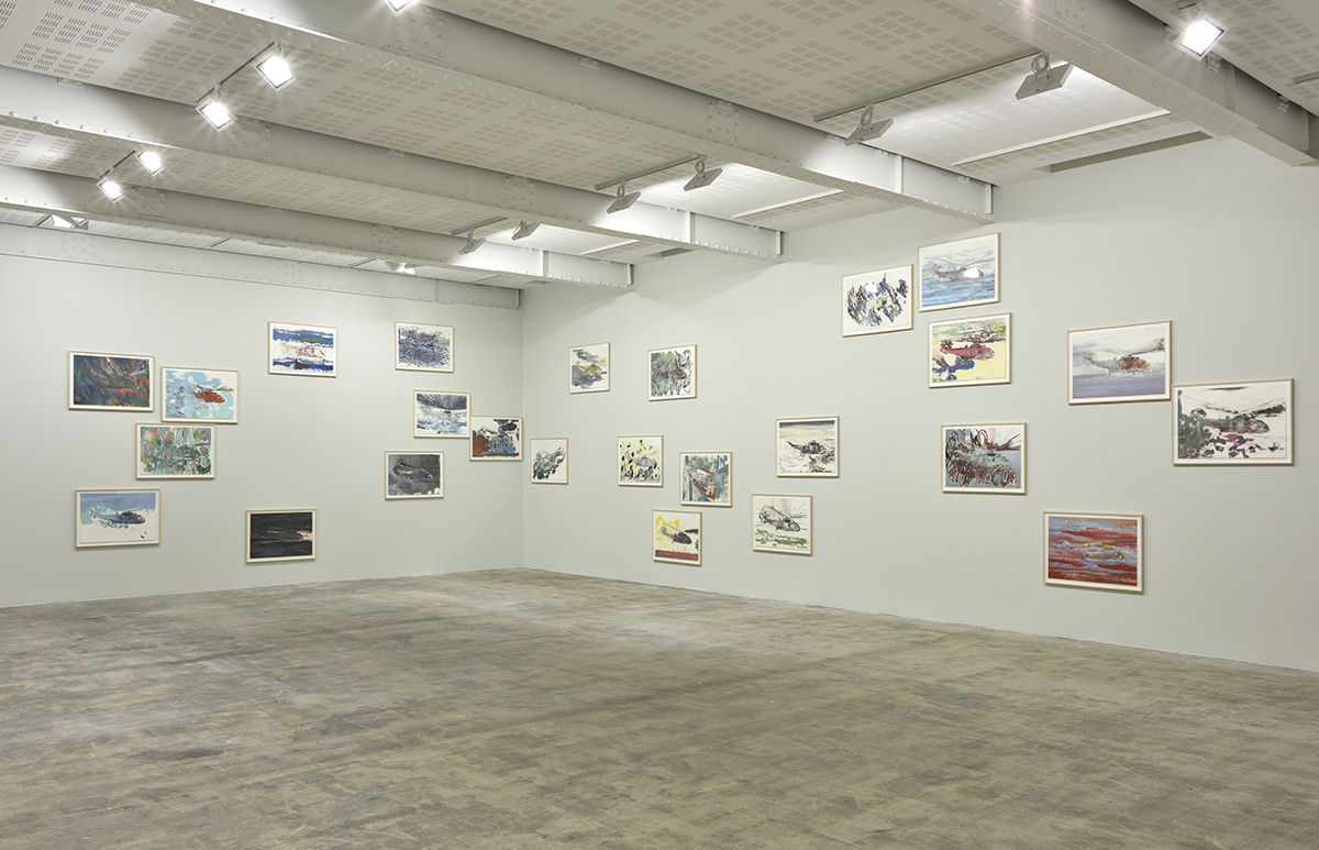 Framed paintings of helicopters on paper hang at various heights on a beige wall.