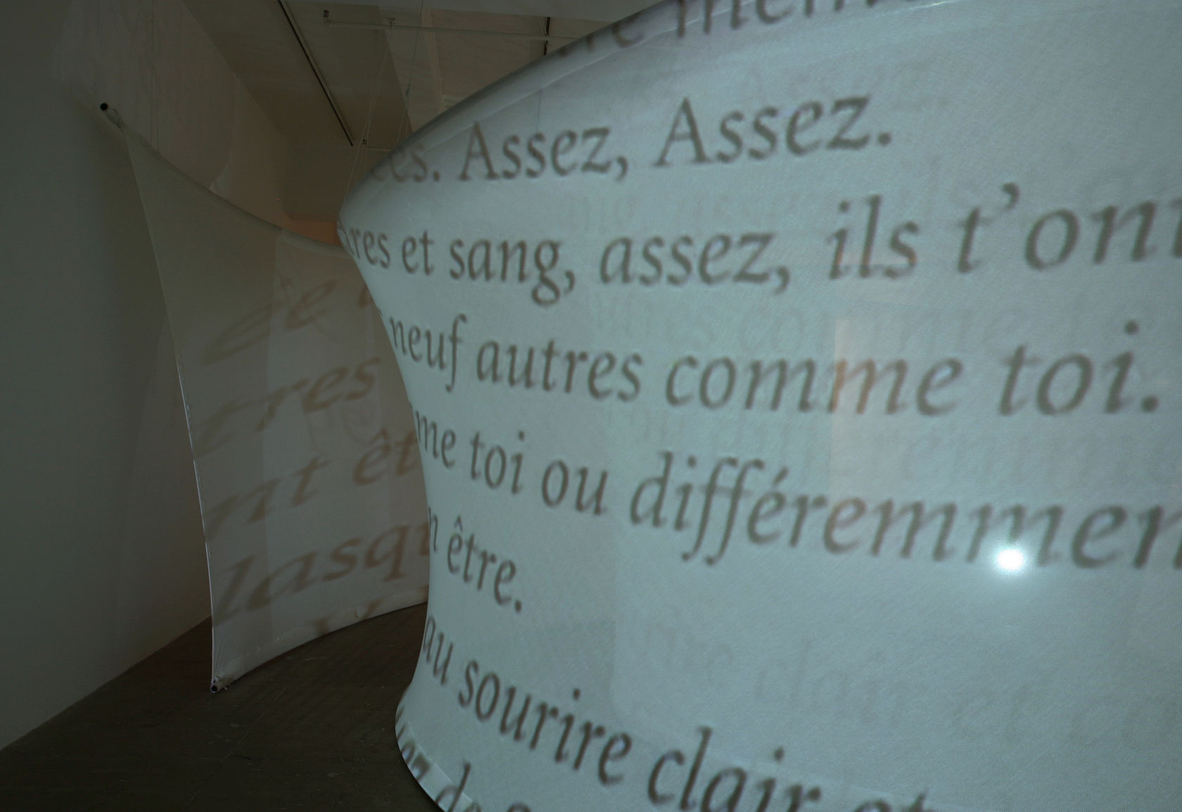 Text in french projected onto a curved, white, translucent piece of fabric stretched from floor to ceiling. 
