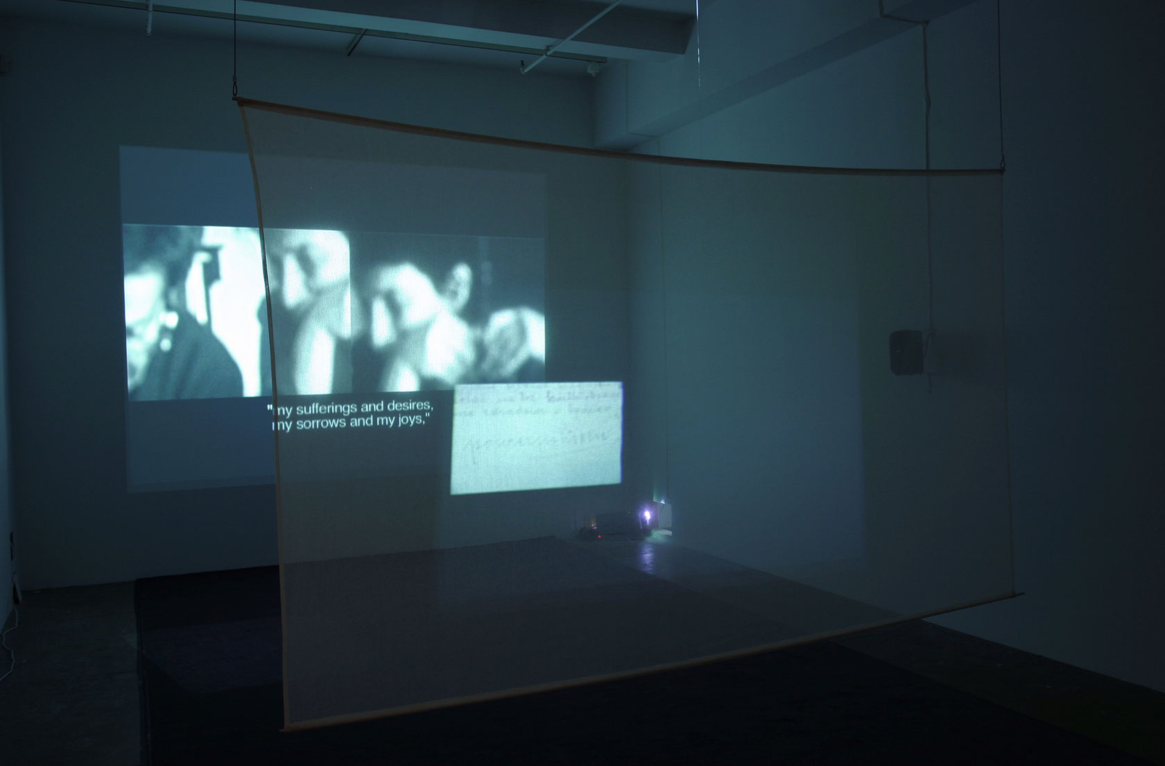 An image of 2 people with subtitles is projected through a transparent piece of fabric onto the wall. 
