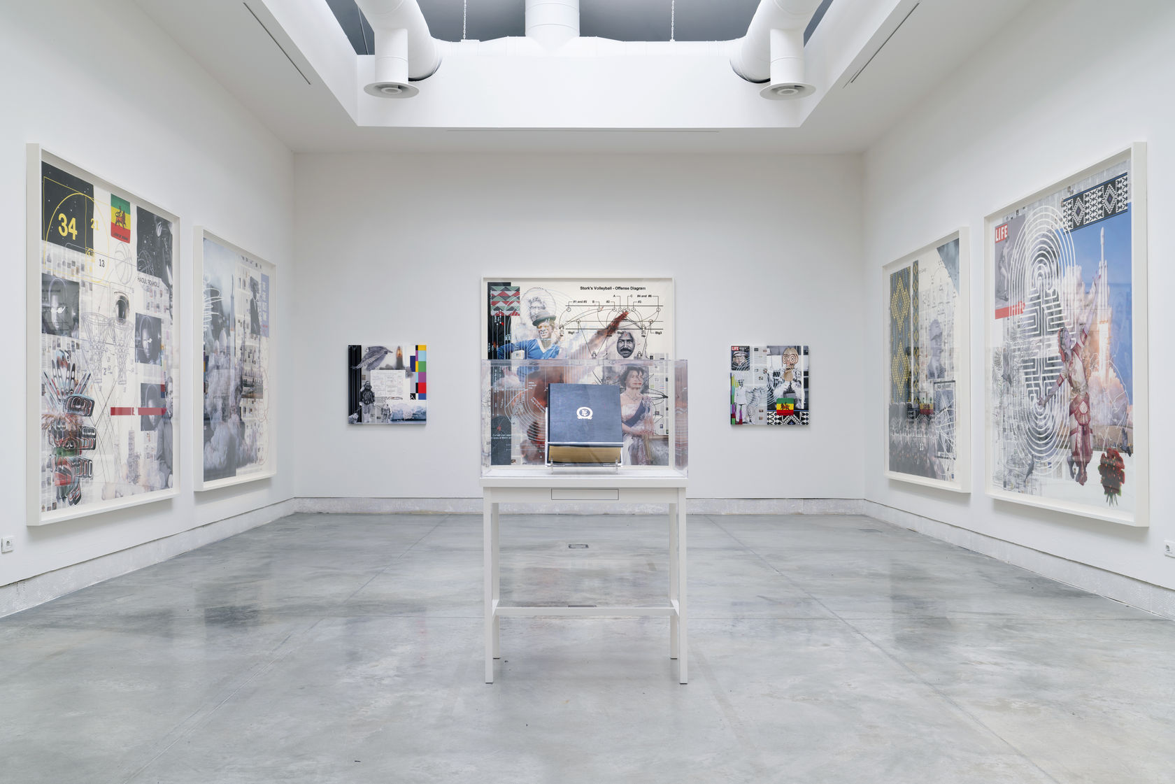 Installation view of an exhibition by Tavares Strachan with large framed works on the wall and a vitrine in the center of the room