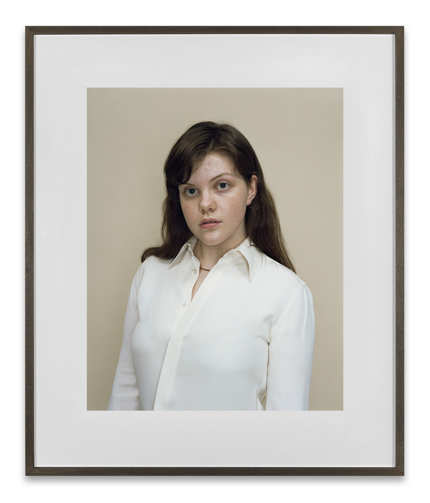 A Rineke Dijkstra portrait of the actress Georgie Henley in a white button down shirt in front of a neutral background. 