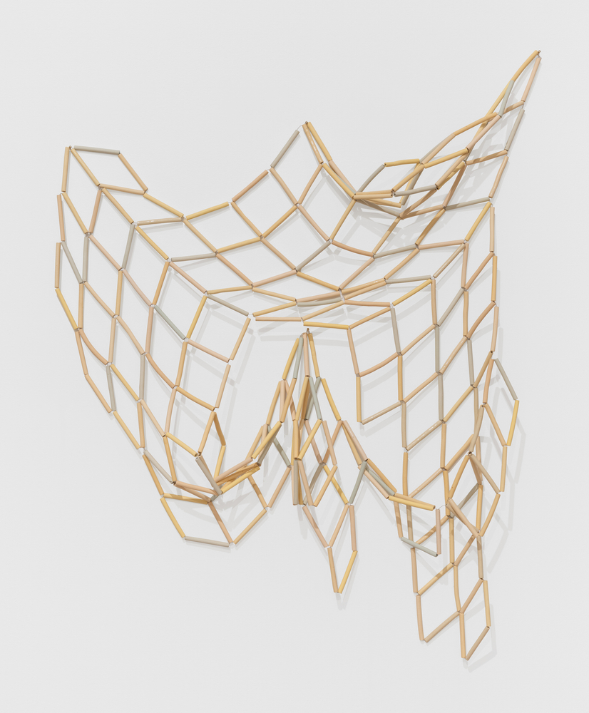 An artwork by Nadia Myre of ceramic tubular beads strung together in diamond sections hung on the wall.