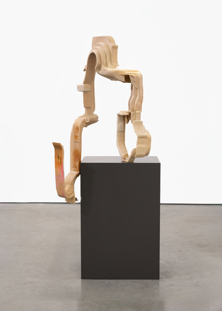 A sculpture by David Armstrong Six made of wood carved into an abstracted geometric form  mounted on a black pedestal.
