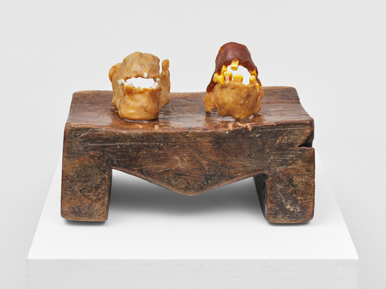 Sculpture depicting one jawbone with pearls affixed to it and one jawbone with corn affixed to it on a wooden base