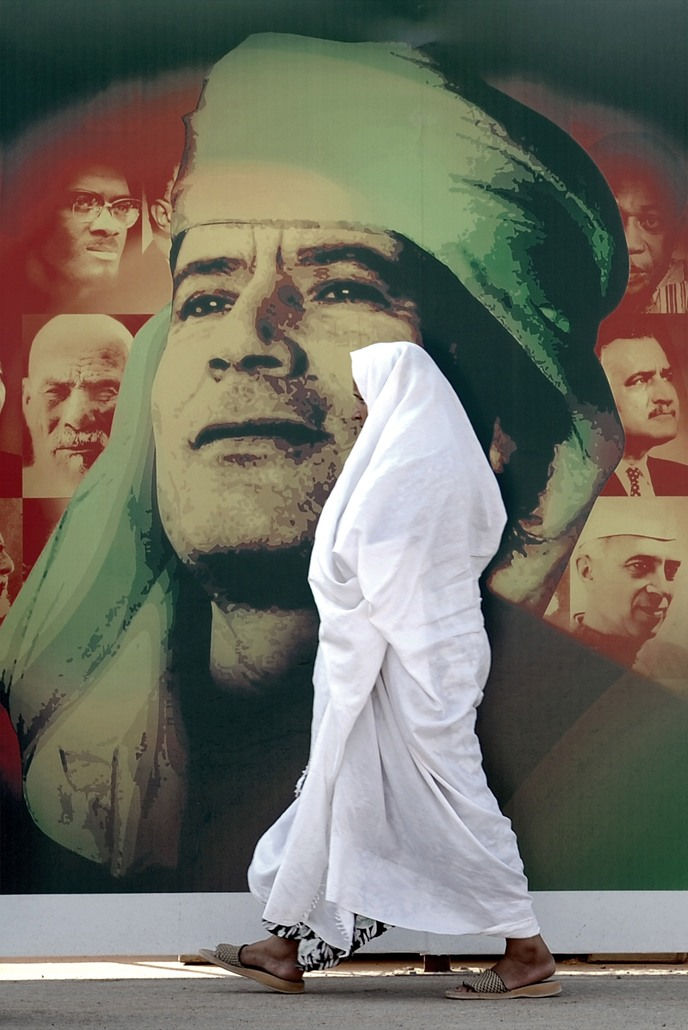 Ammar Abd Rabbo, A woman passes a giant poster of Libyan leader Muammar Gaddafi in Tripoli, a day before the 40th anniversary of "Al Fateh" revolution, 2009