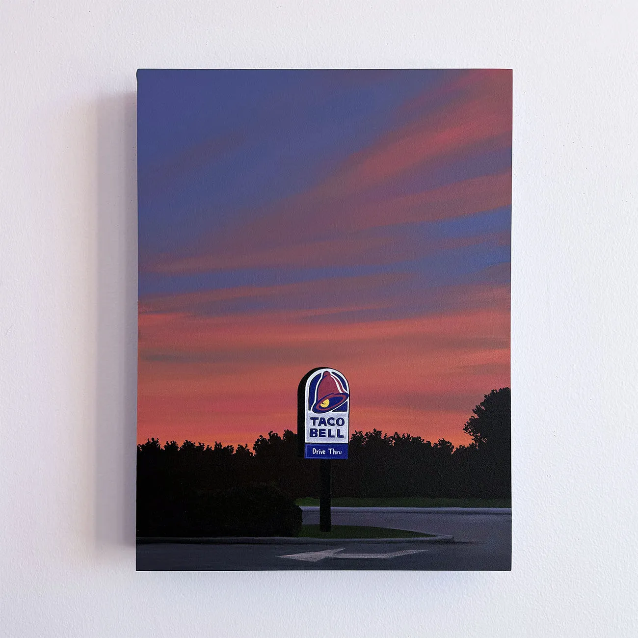 Kristin Moore Taco Bell Sunset painting featuring a roadside Taco Bell sign at dusk with a vivid red and purple sky and silhouetted trees. Hanging on a white wall