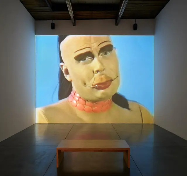 Video projection in a darkened art gallery - Leigh Bowery against a light blue background