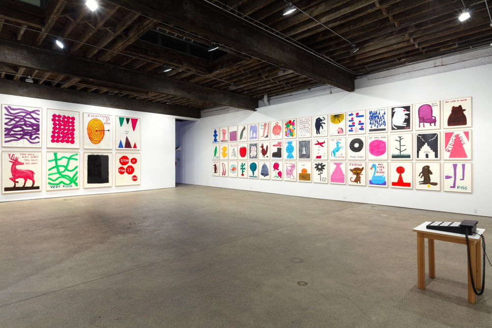 Installation view of David Shrigley's sixth solo show at Anton Kern Gallery, featuring 78 new drawings, two sculptures, an animation, and some humor. A third wall of works.