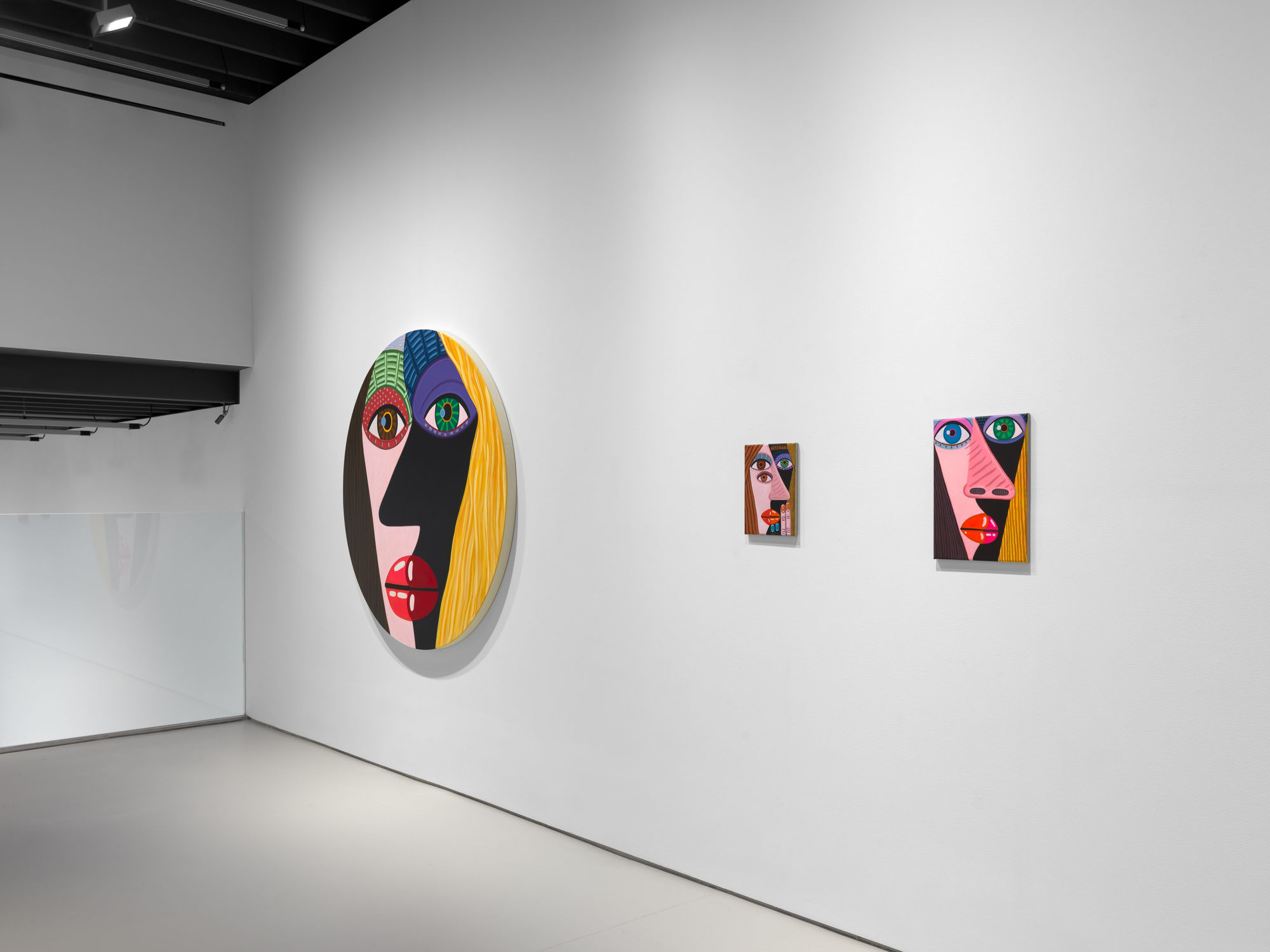 installation view of Brian Calvin's Waiting featuring paintings with hyperbolic color, mosaic eyes, and more. Two small rectangular works next to one of Calvin's circle canvases.