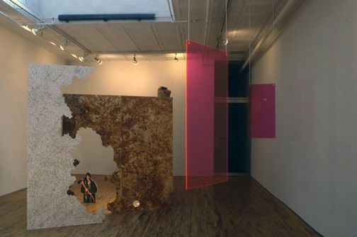 Installation view of Lothar Hempel's show titled "America Disappears Only the Smile Remains," featuring plexiglass works, wood cutouts, and other photocollages. Hanging plexiglass and wooden work featured.